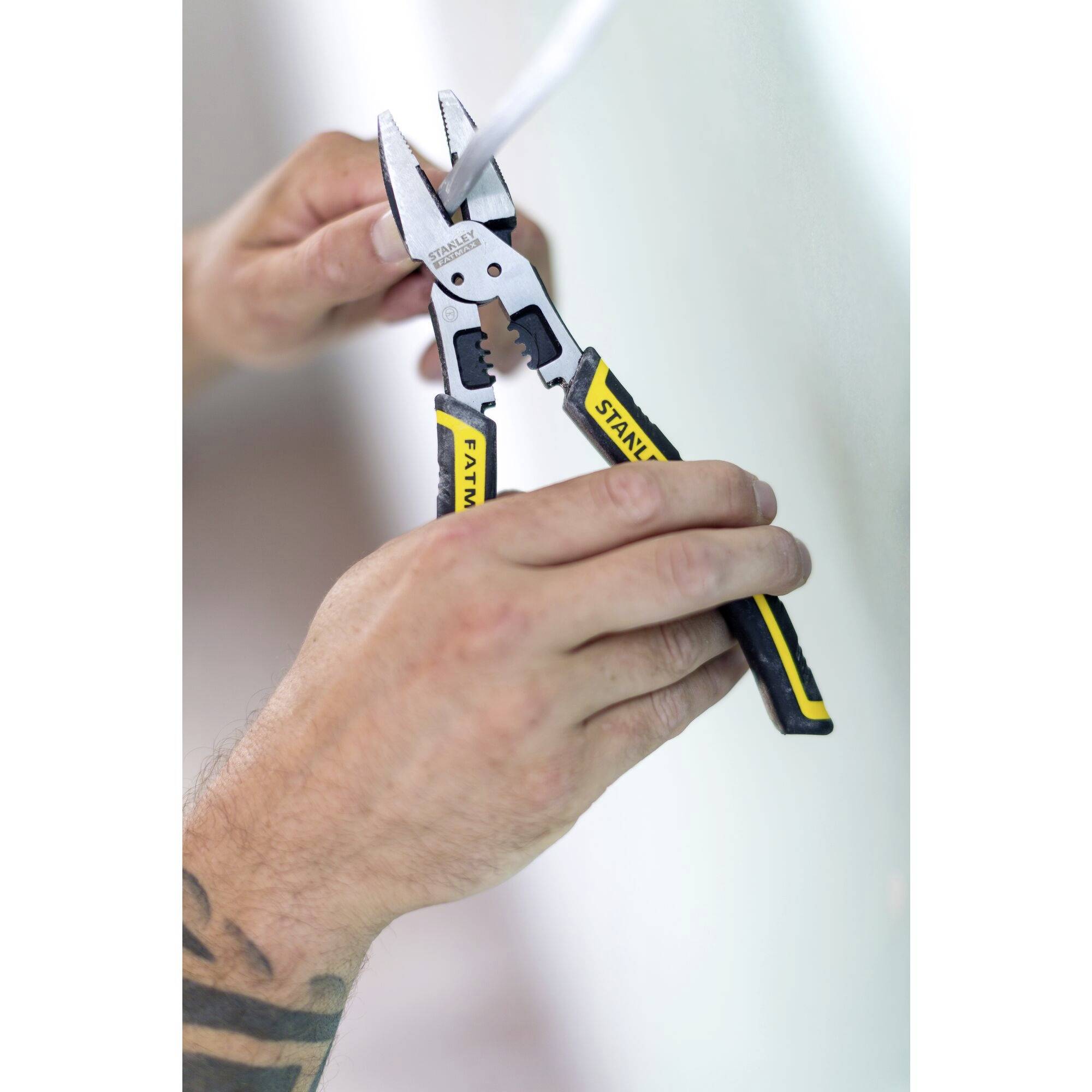 Osoba używa szczypiec do ściągania izolacji z przewodu. Fokus jest skierowany na dłonie i narzędzie.