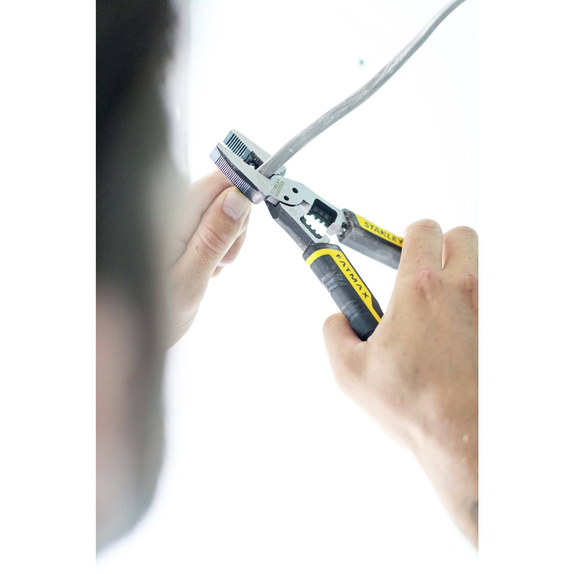 Osoba używa szczypiec do zdejmowania izolacji z kabla. Ręce precyzyjnie trzymają narzędzie, podczas gdy kabel jest unieruchomiony.