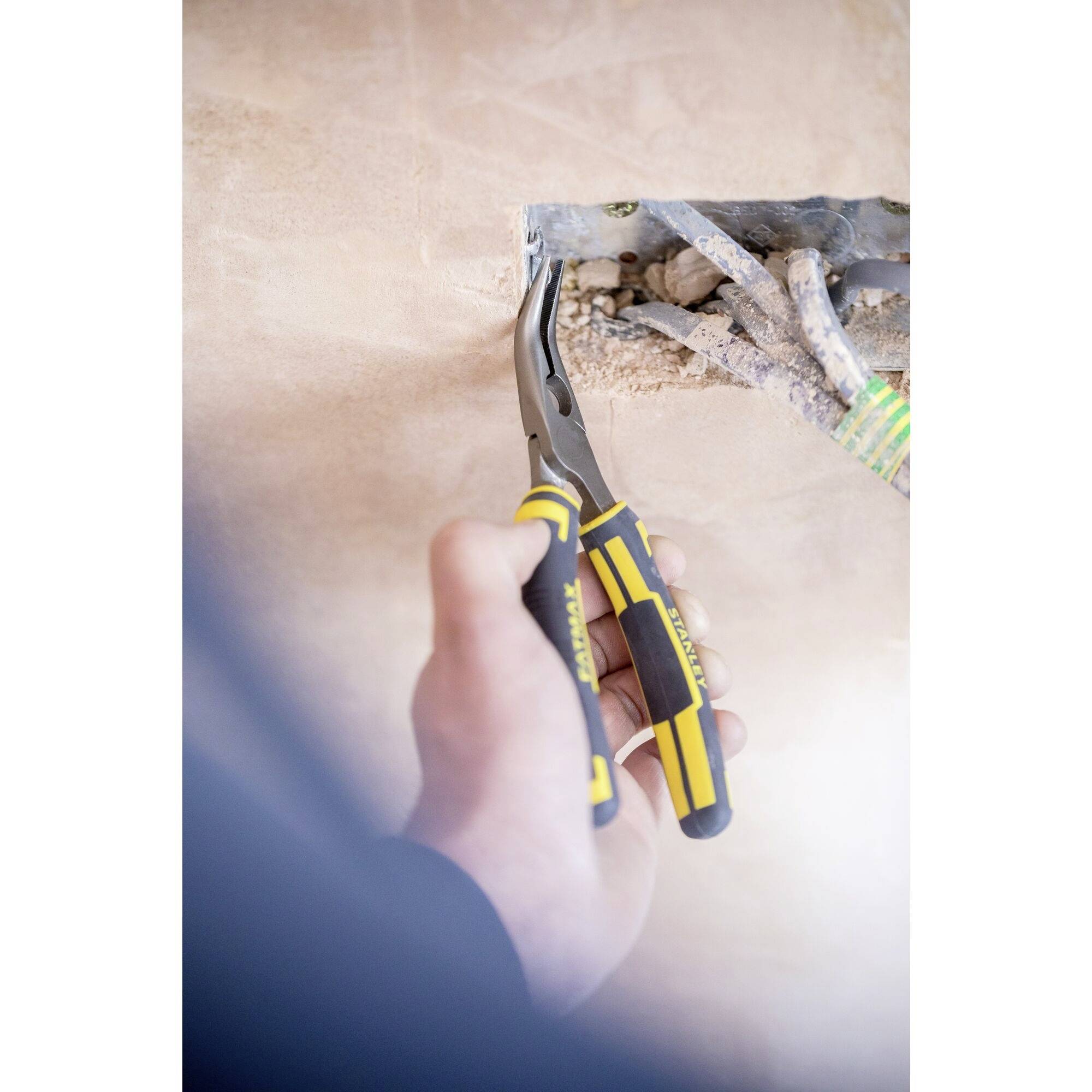 Jedna ręka trzyma szczypce i pracuje przy przewodach elektrycznych w otworze ściennym. Obraz przedstawia proces naprawy lub instalacji.