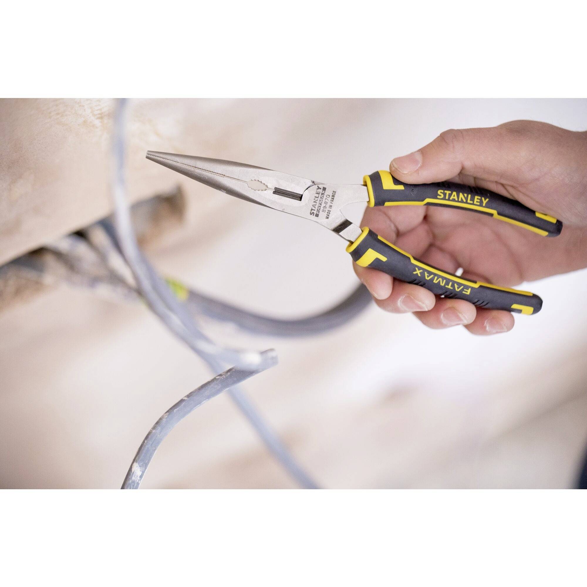 Ręka trzyma kombinerki Stanley i przecina niebieski przewód. Szczypce mają czarne uchwyty z żółtymi akcentami.
