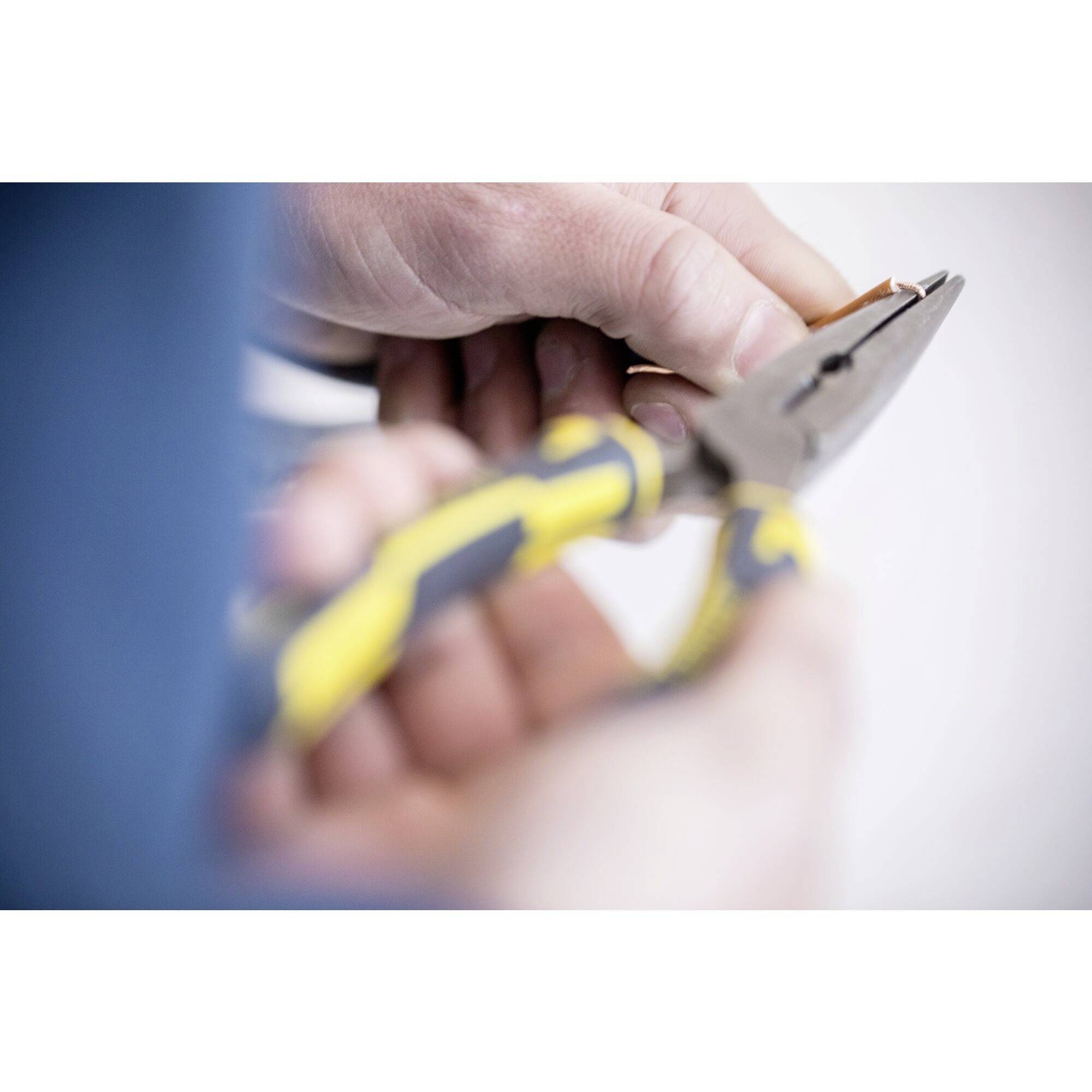 Osoba trzyma szczypce z żółtą rączką, gotowa do cięcia lub naprawy.