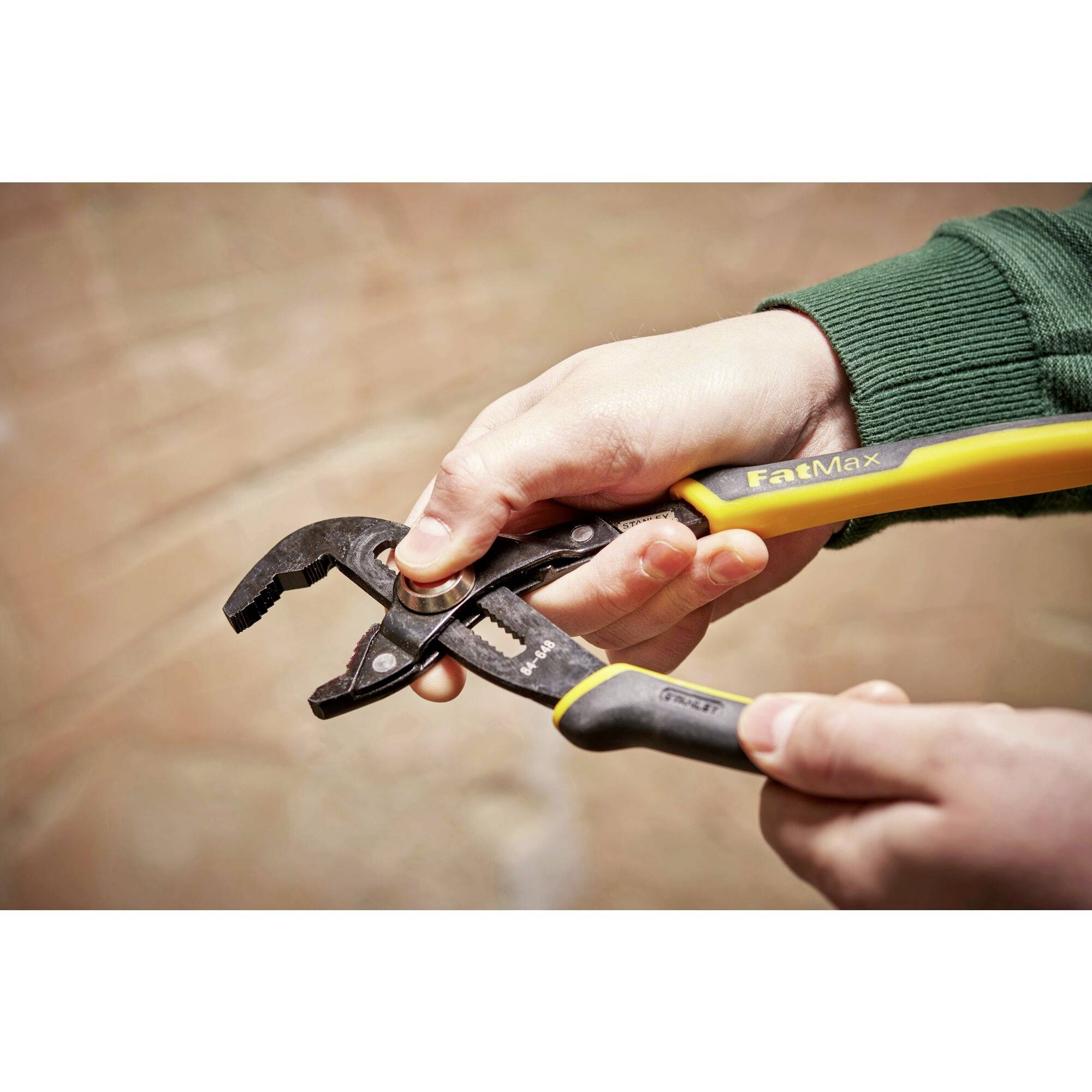 Osoba trzyma regulowaną szczypce z żółto-czarnym uchwytem, gotowa do ich użycia. Ręce i narzędzie są w centrum uwagi.