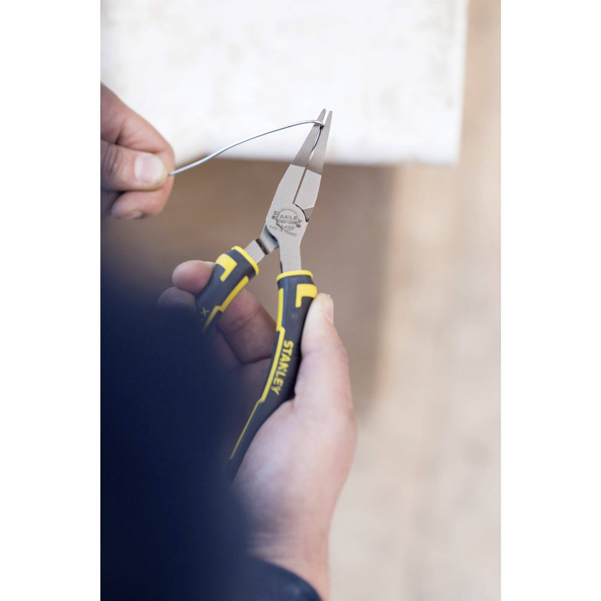 Osoba przecina kawałek drutu szczypcami. Ręka trzyma drut blisko czubków szczypiec.