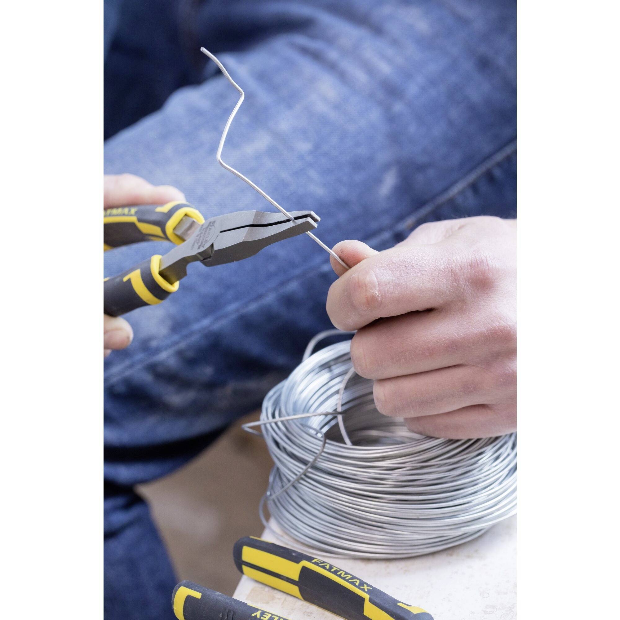 Osoba przecina kawałek drutu szczypcami z dużej rolki leżącej na stole.