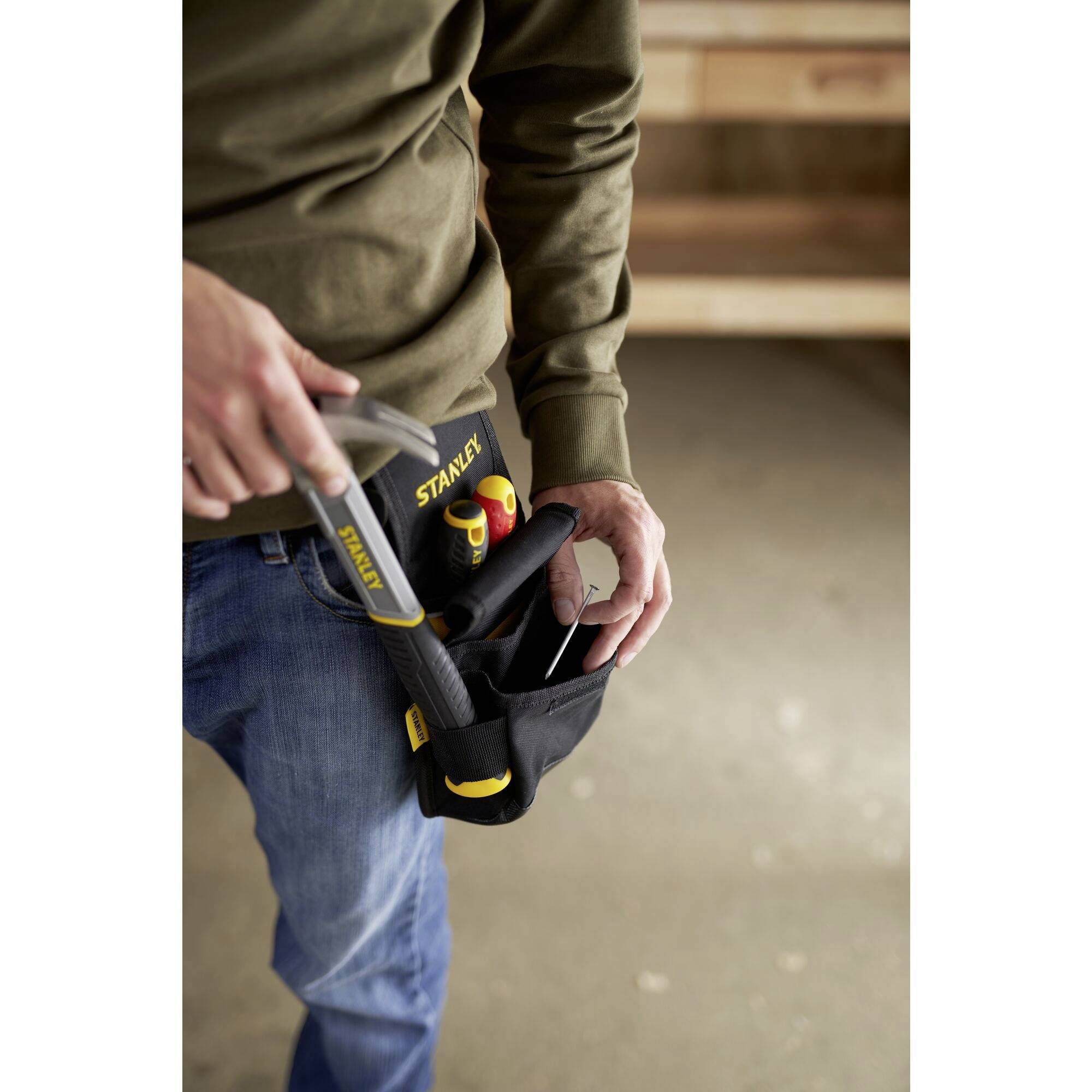Rzemieślnik niesie czarną torbę narzędziową z młotkiem i innymi narzędziami, które są właśnie wyjmowane.