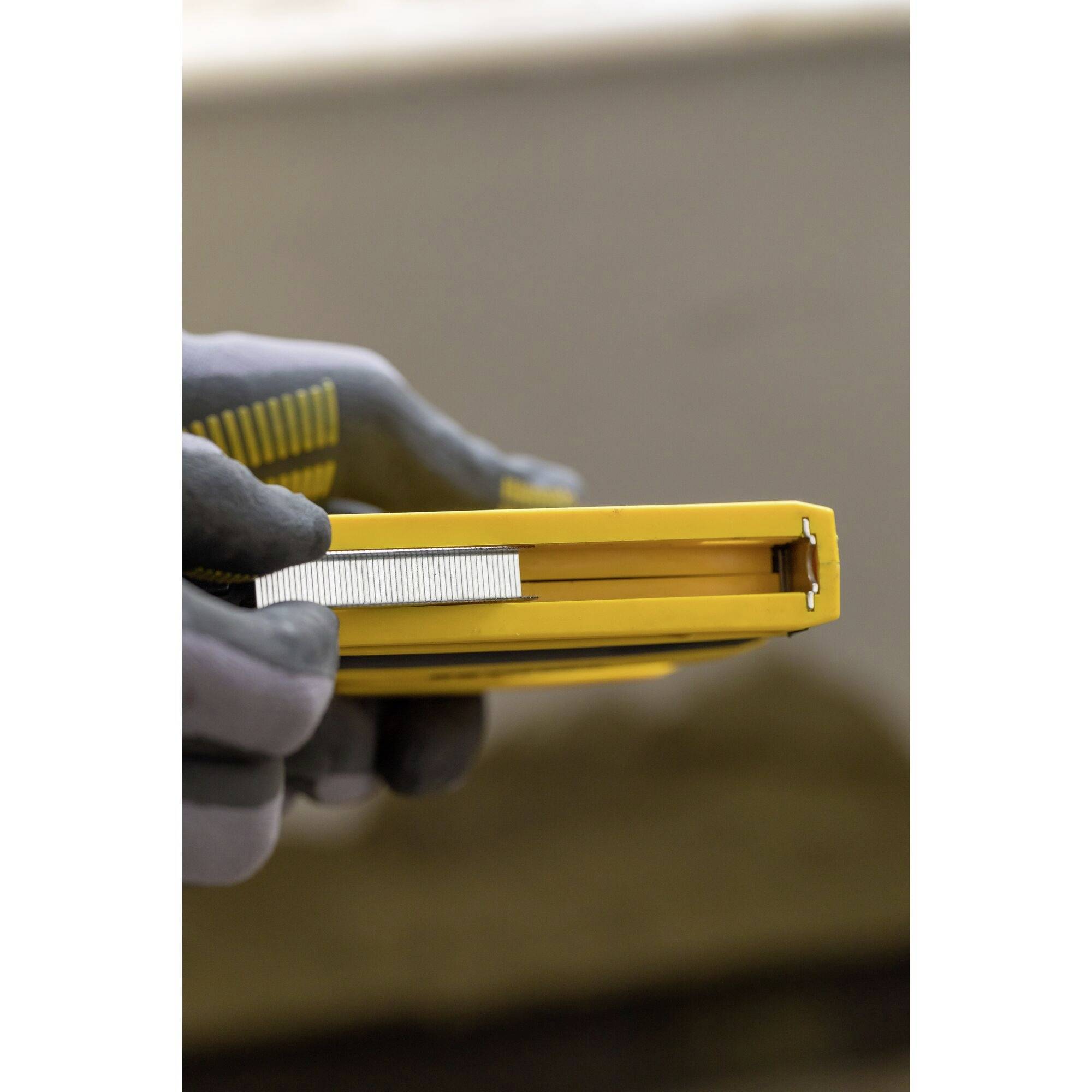 Osoba trzyma żółtą taśmę mierniczą, częściowo wysuniętą, w szarych rękawicach roboczych.