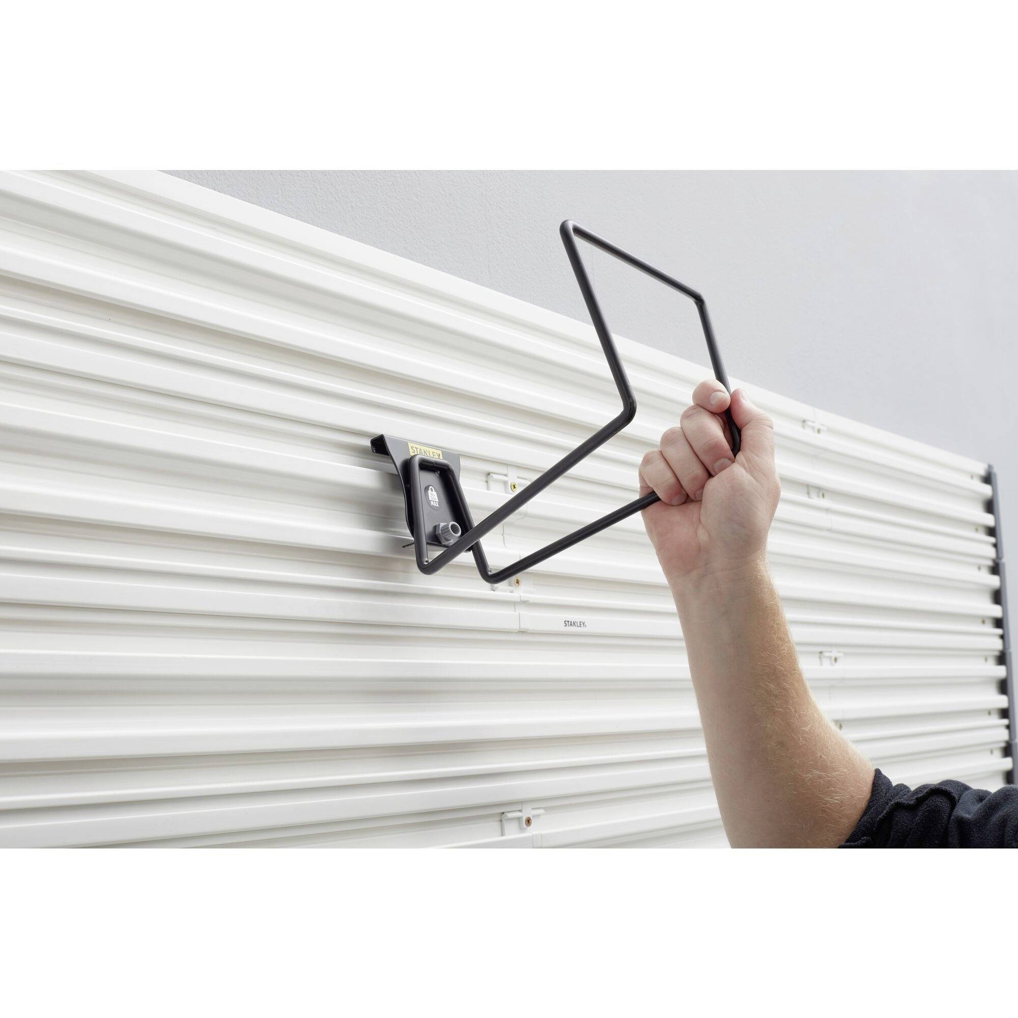 Osoba montuje czarny, prostokątny uchwyt na białej, prążkowanej ścianie, prawdopodobnie w celu zamocowania jakiegoś przedmiotu.
