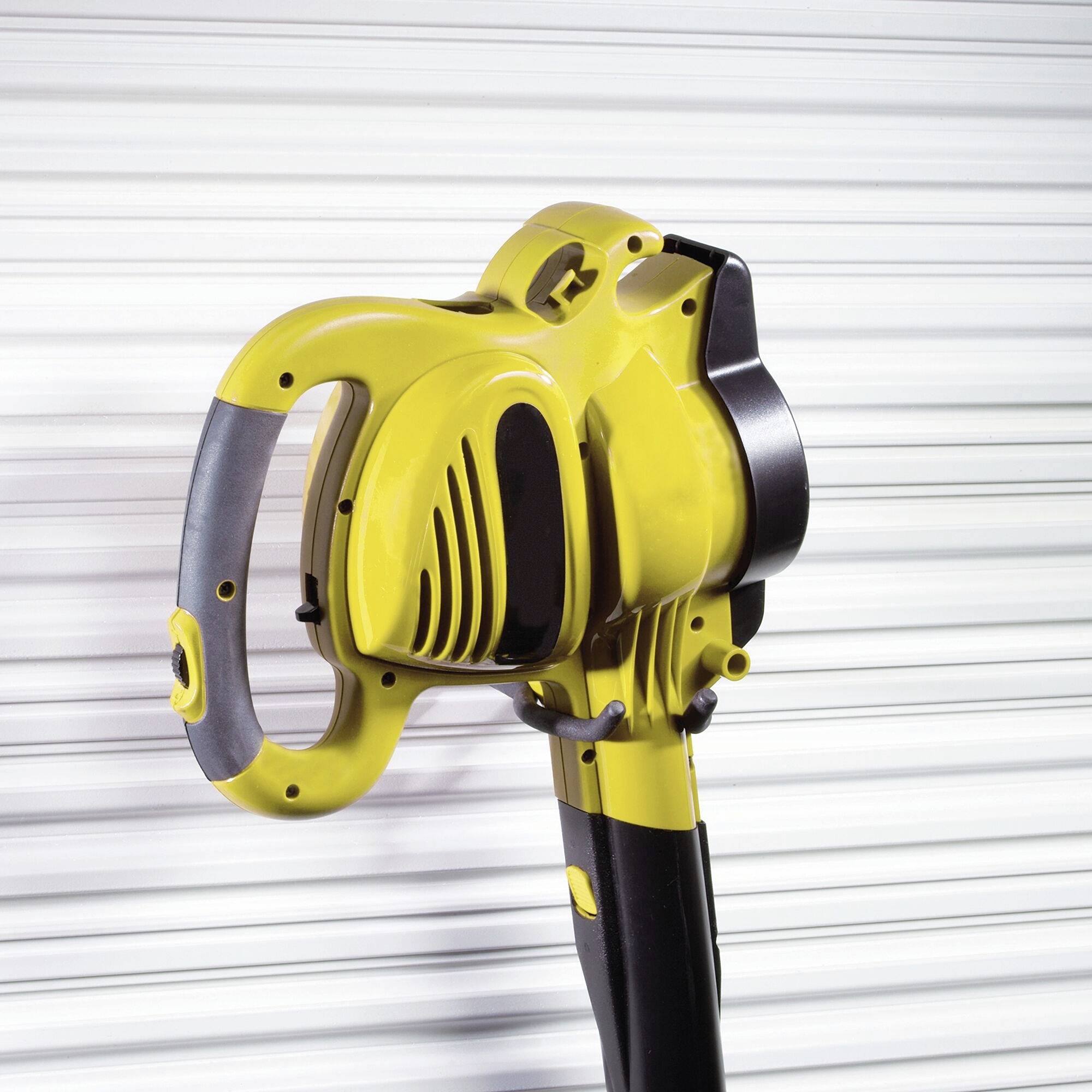 Żółty odkurzacz do liści stoi pionowo na rozmytym tle. Urządzenie posiada ergonomiczny uchwyt i kompaktową budowę.