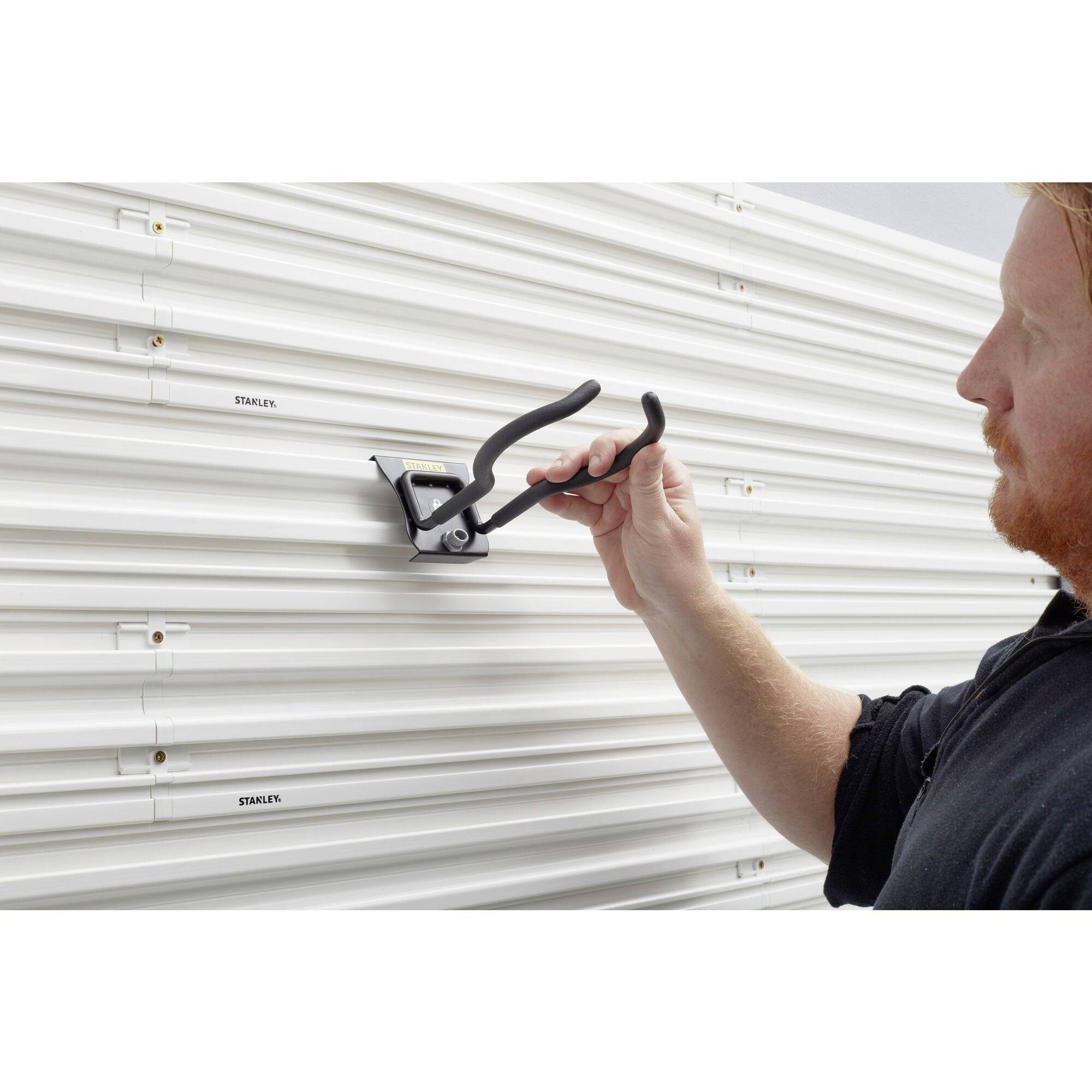 Rzemieślnik mocuje czarny hak do przechowywania na żebrowanej białej ścianie metalowej, prawdopodobnie przeznaczony do narzędzi lub sprzętu.