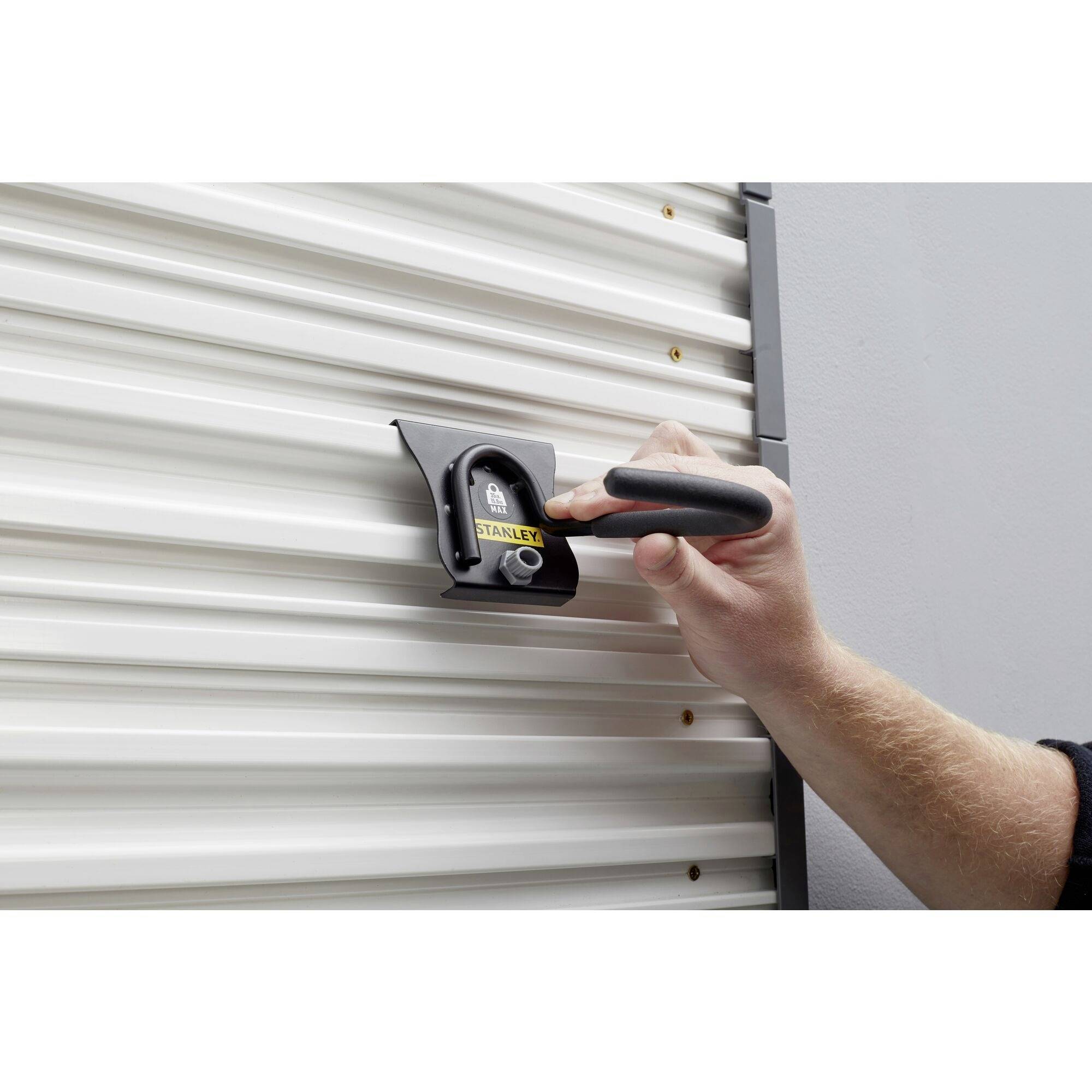 Jedna ręka trzyma kłódkę przy prążkowanej metalowej bramie. Kłódka wydaje się być zabezpieczona w urządzeniu ryglowym.