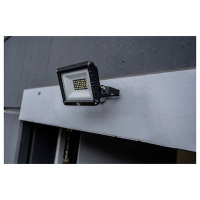 Czarny reflektor LED zamontowany na ciemnej ścianie zewnętrznej powyżej srebrnego panelu metalowego.