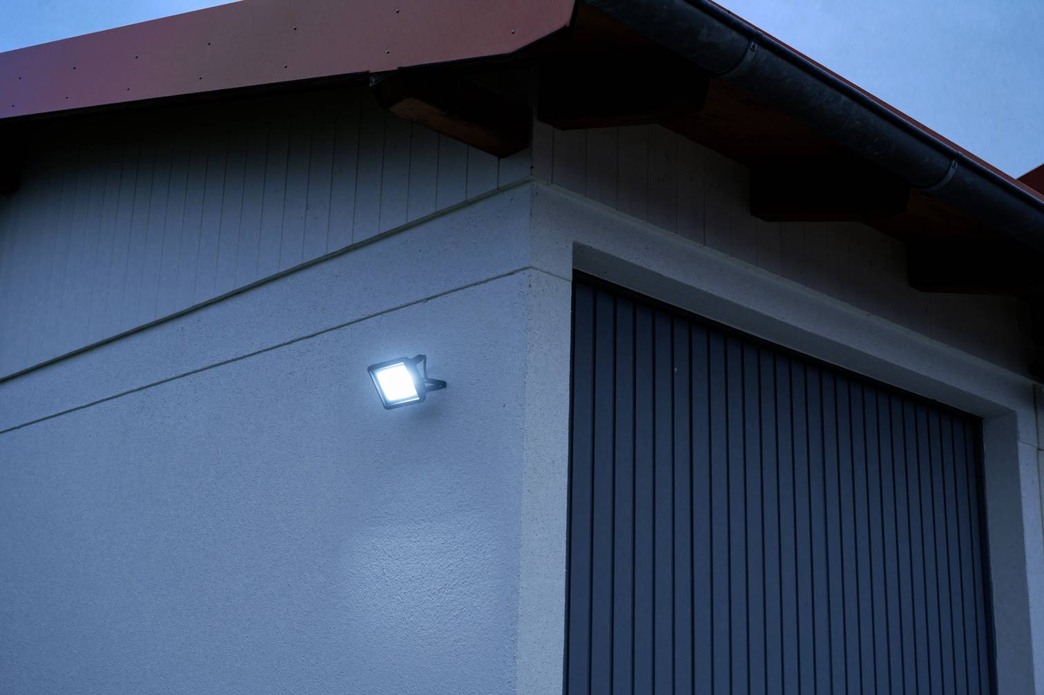 Widok z zewnątrz budynku o zmierzchu. Na ścianie świeci jasny reflektor LED, oświetlając budynek.