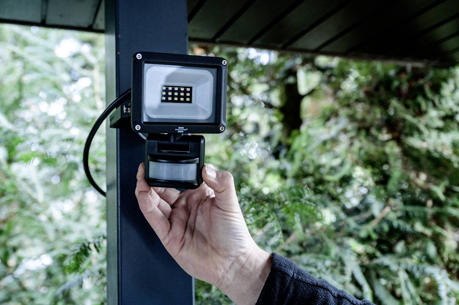 Osoba instaluje lub reguluje LED-owy reflektor zewnętrzny z czujnikiem ruchu na słupie na wolnym powietrzu.