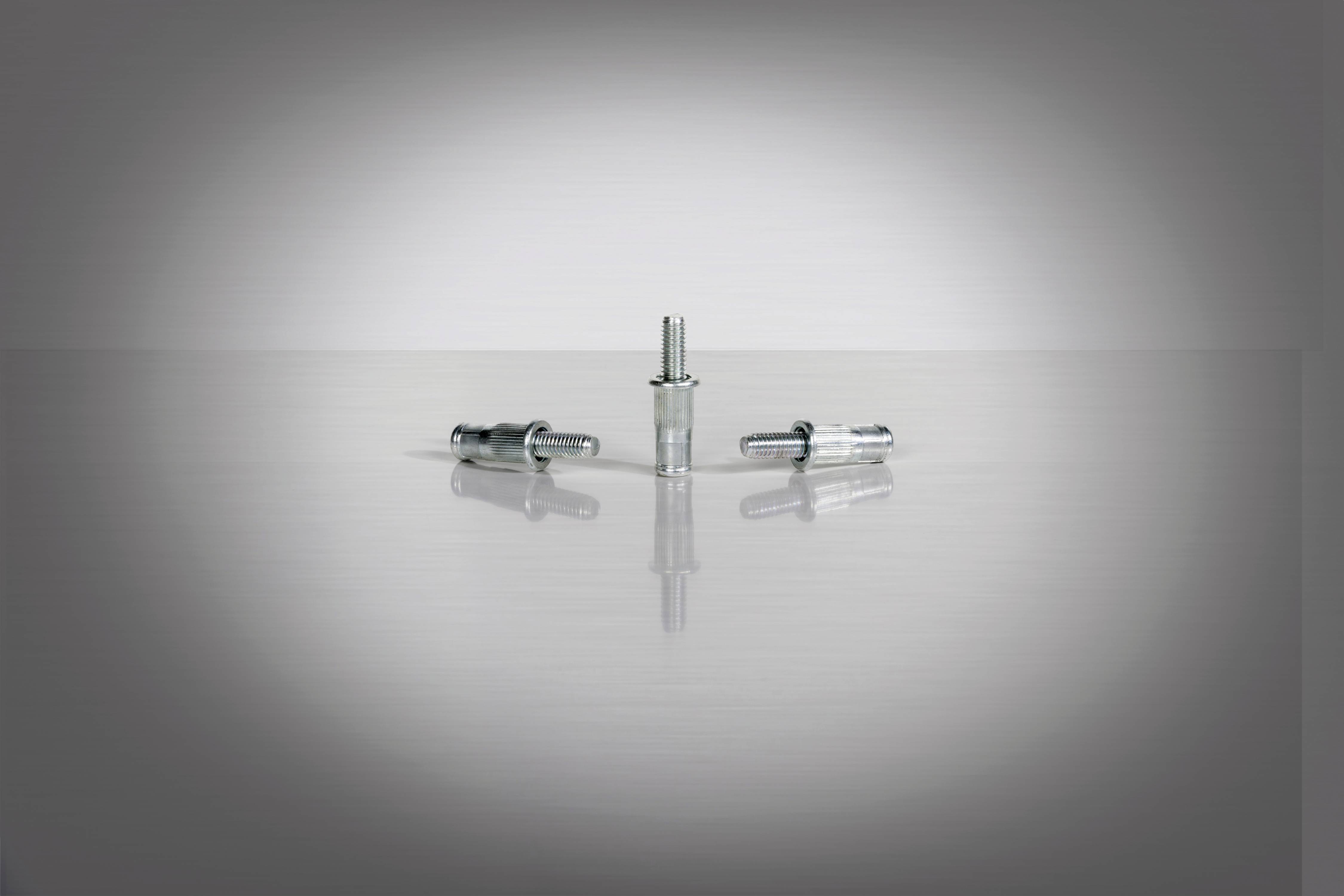 Trzy srebrne śruby na błyszczącej powierzchni, rozmieszczone symetrycznie, z jedną śrubą centralnie i dwiema ukośnie obok niej.
