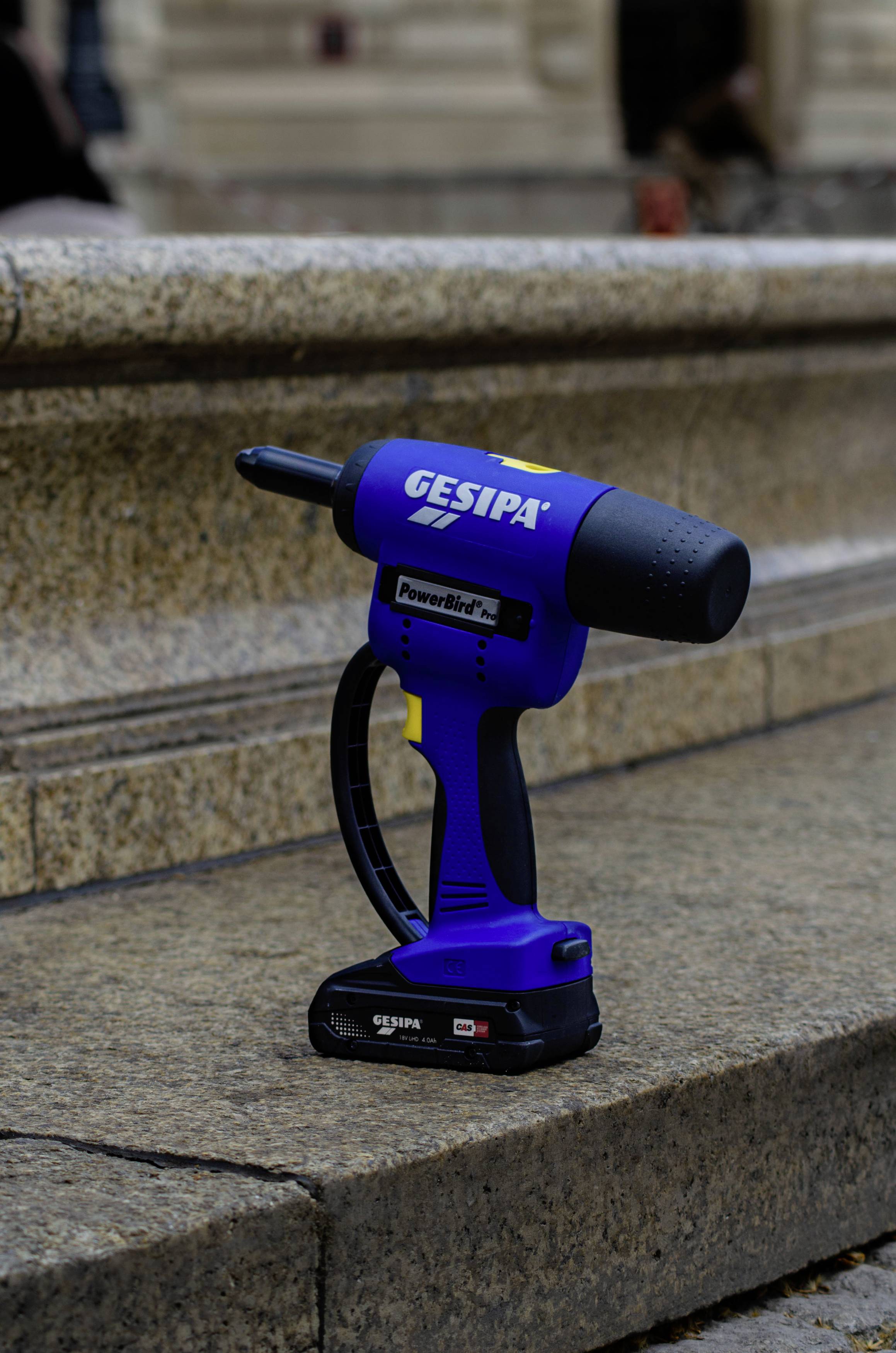 Akumulatorowe narzędzie do nitowania firmy GESIPA, umieszczone na kamiennych schodach na wolnym powietrzu.