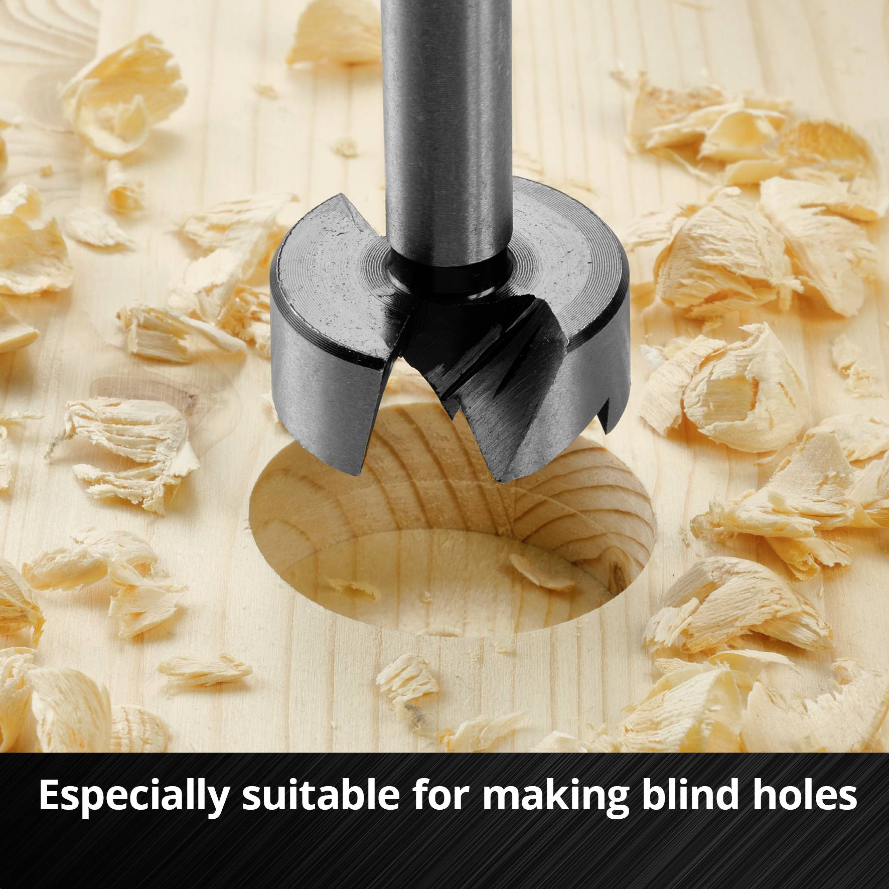 Metalowy wiertarz do drewna w akcji, wwierca okrągły otwór w drewnie, otoczony wiórami. Tekst: 'Szczególnie przydatny do wykonywania otworów przelotowych'.