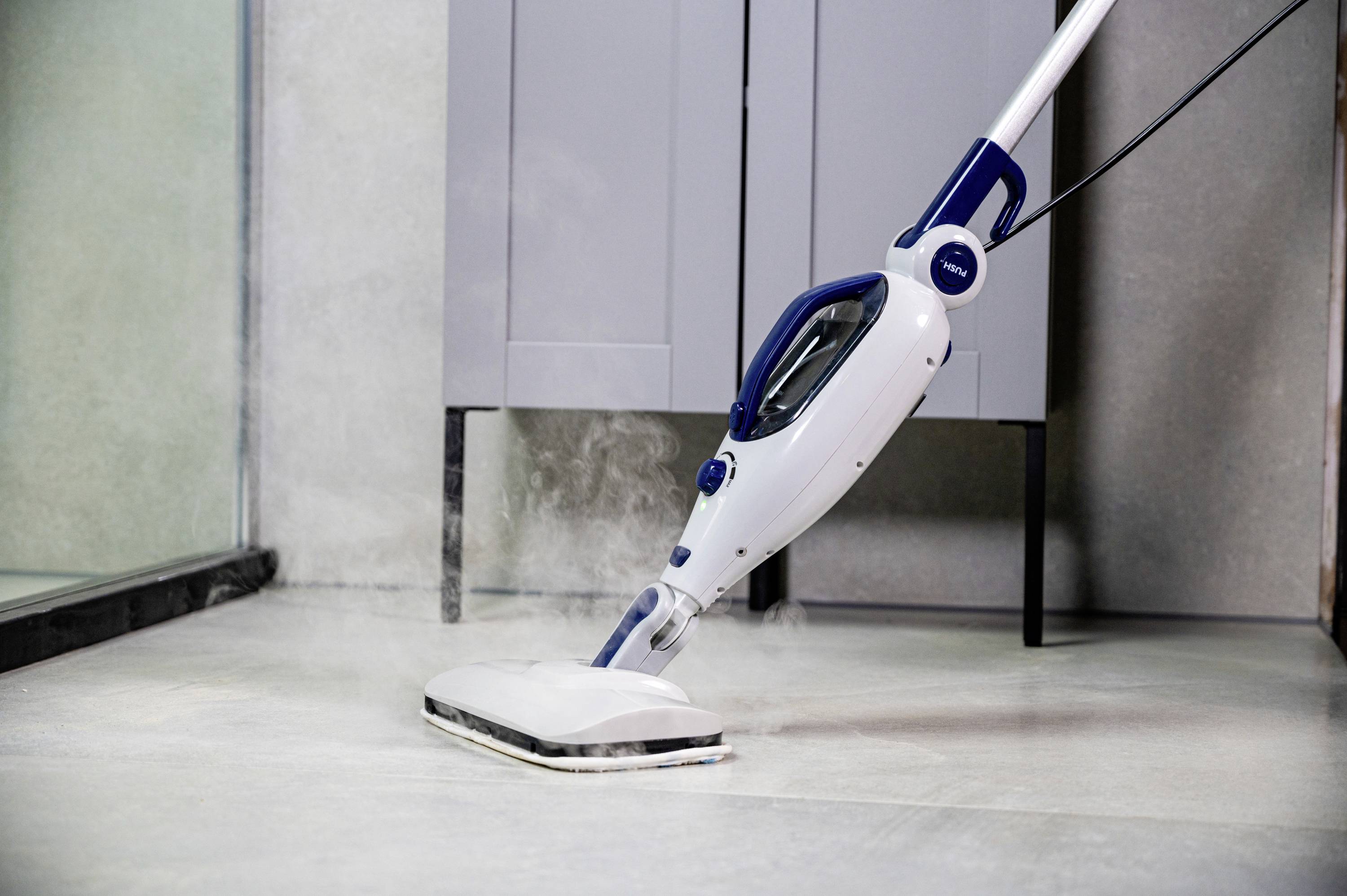 Czyścik parowy czyści szare płytki w nowoczesnej łazience. Cienka para unosi się nad białym urządzeniem czyszczącym.