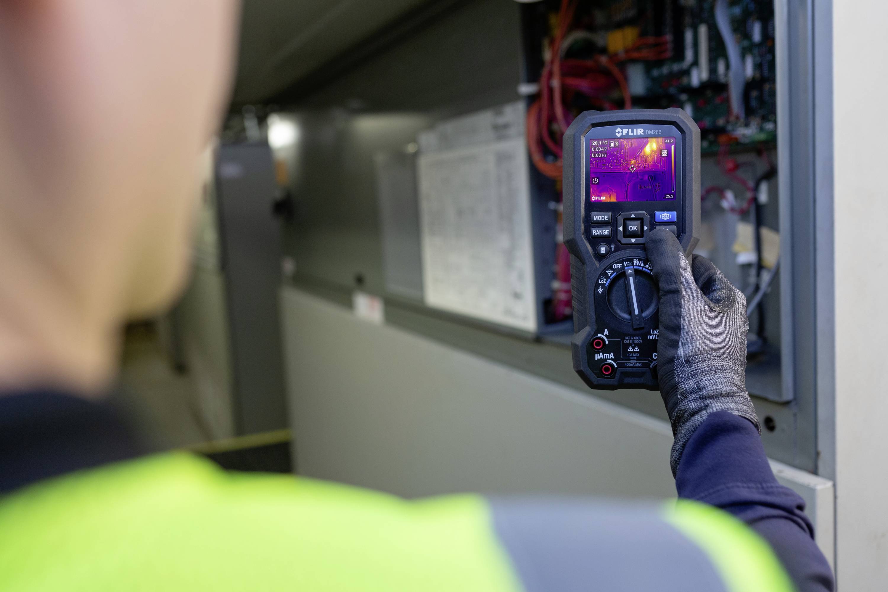 Technik w odzieży ochronnej sprawdza komponenty elektryczne szafy sterowniczej za pomocą kamery termowizyjnej.