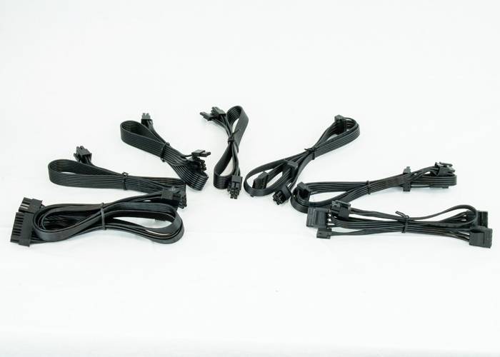 Kilka czarnych kabli komputerowych różnego rodzaju i długości na białym tle, w tym przewody zasilające i transmisji danych.