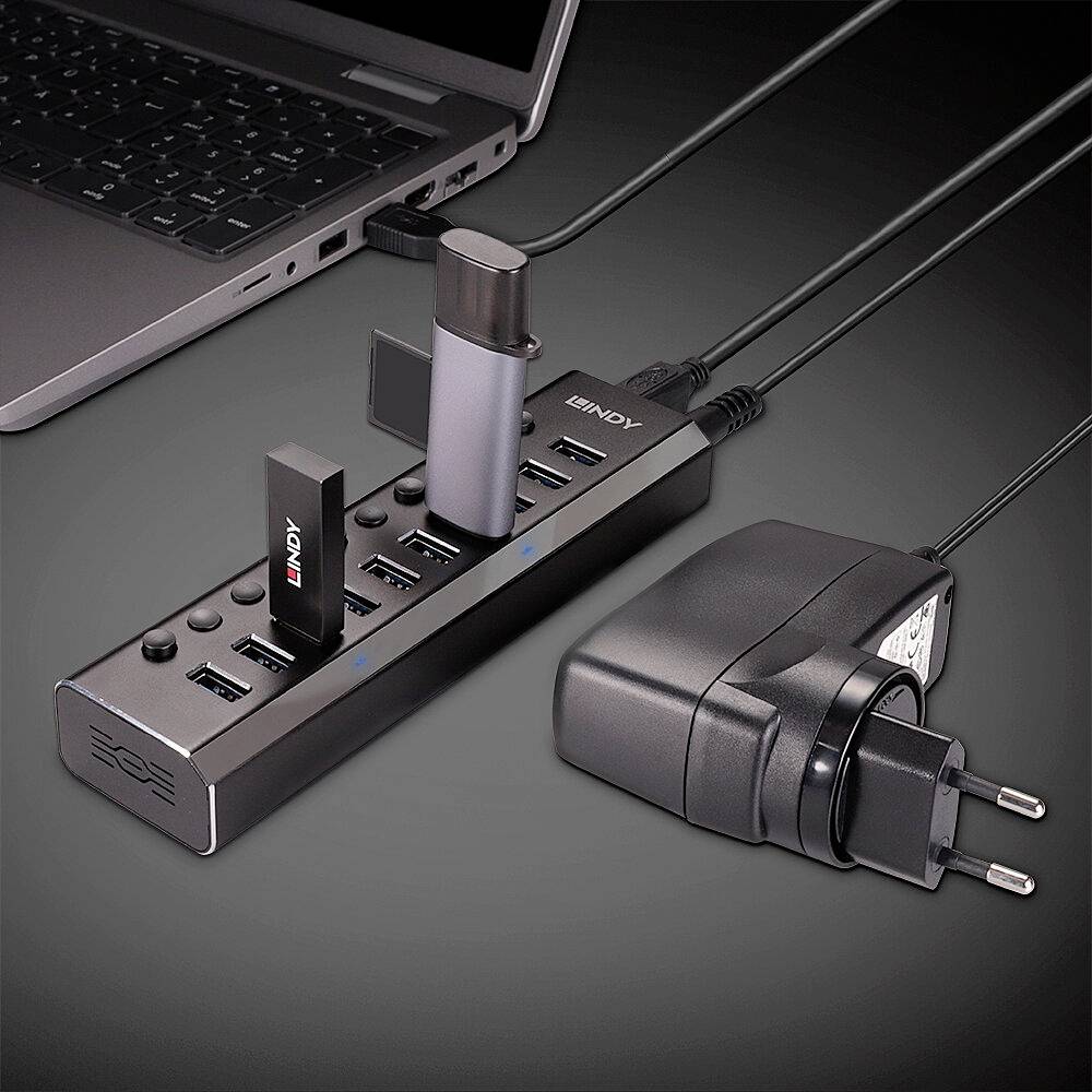 Koncentrator USB z ośmioma portami, podłączony do laptopa. Dwa urządzenia są podłączone. Obok leży zasilacz sieciowy.