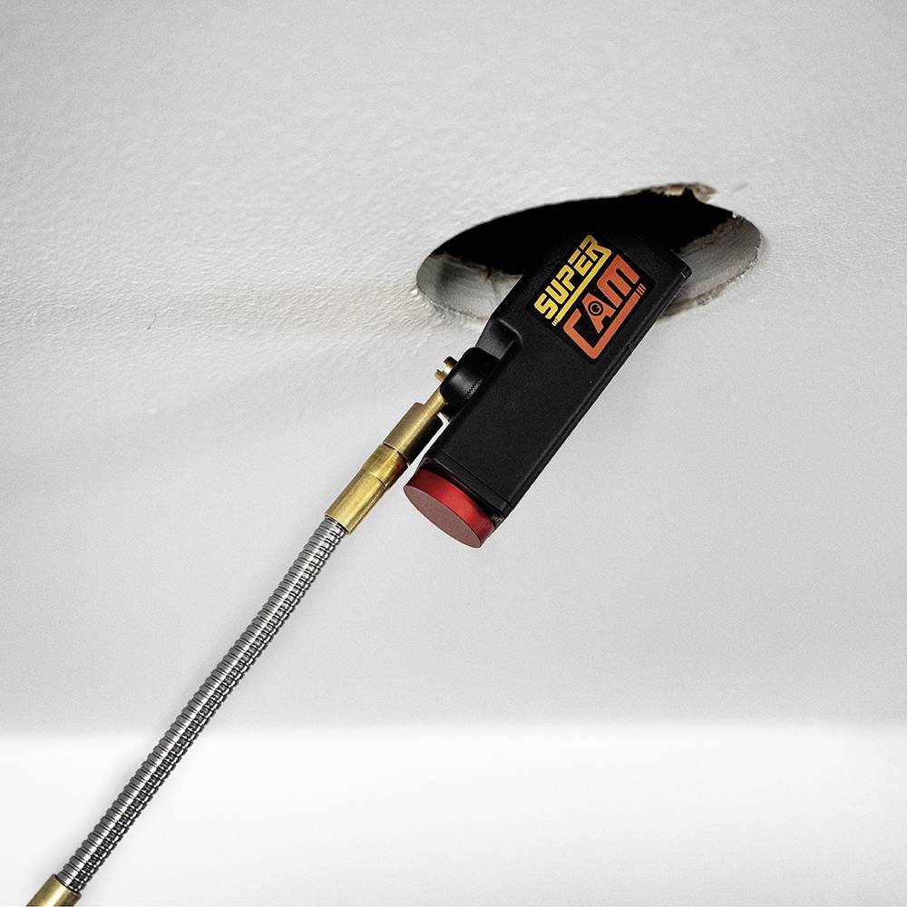 Kamera inspekcyjna jest wprowadzana przez otwór w suficie. Kamera jest oznaczona jako 'SupCam'.