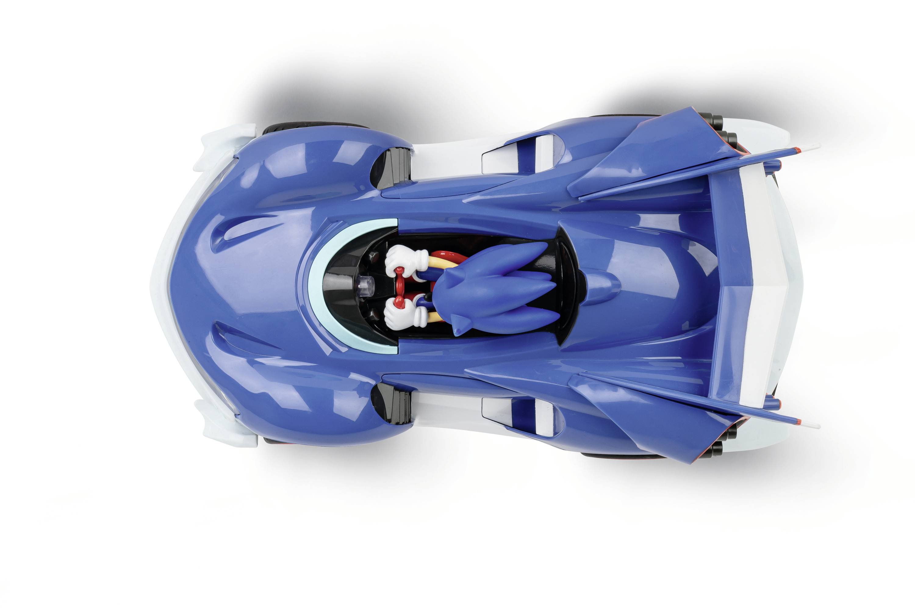 Niebieskie autko zabawkowe z skrzydłami i czerwoną pokrywą kokpitu, widziane z góry. W pojeździe siedzi stylizowana postać.