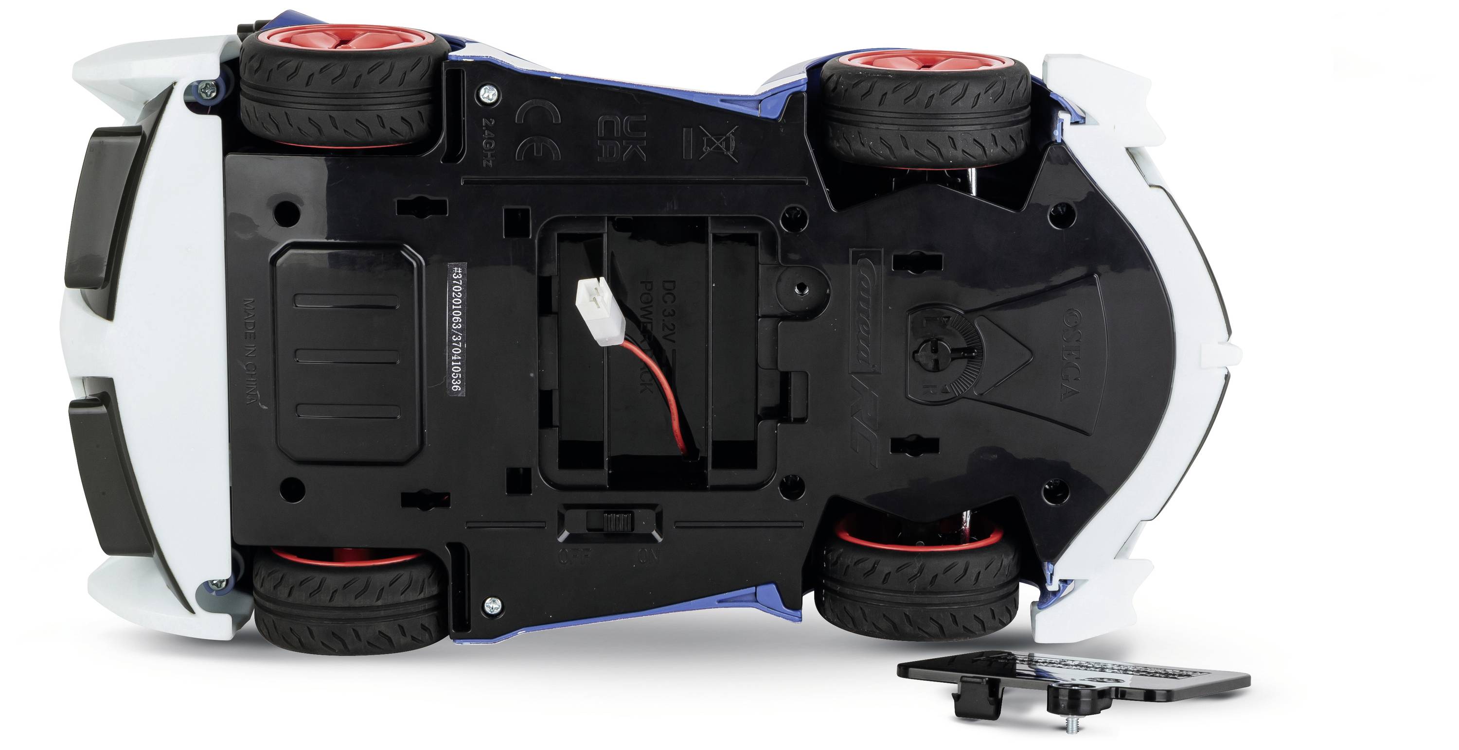 Zabawkowy samochodzik przewrócony do góry nogami, ukazujący spód z widoczną komorą baterii i podniesioną podporą.