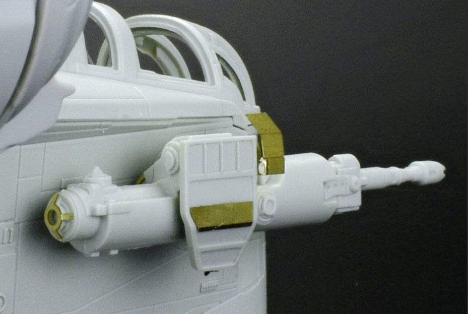 Zbliżenie lufy armaty samolotowej ze złotymi detalami. Jest zamontowana na jasnoszarym kadłubie samolotu.