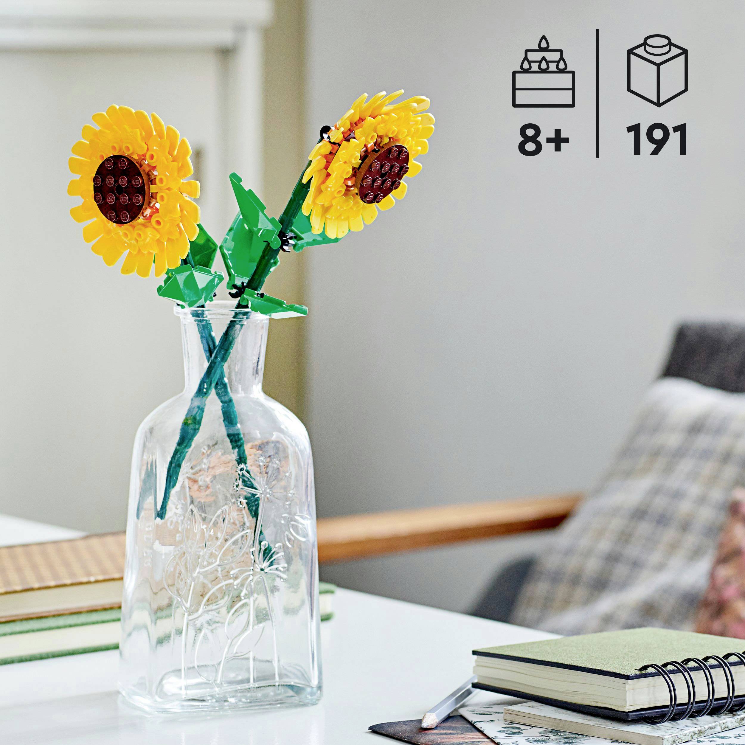 Dwie żółte słoneczniki z klocków Lego stoją w szklanym wazonie na stole obok notatnika. W prawym górnym rogu symbole: od 8 lat, 191 elementów.