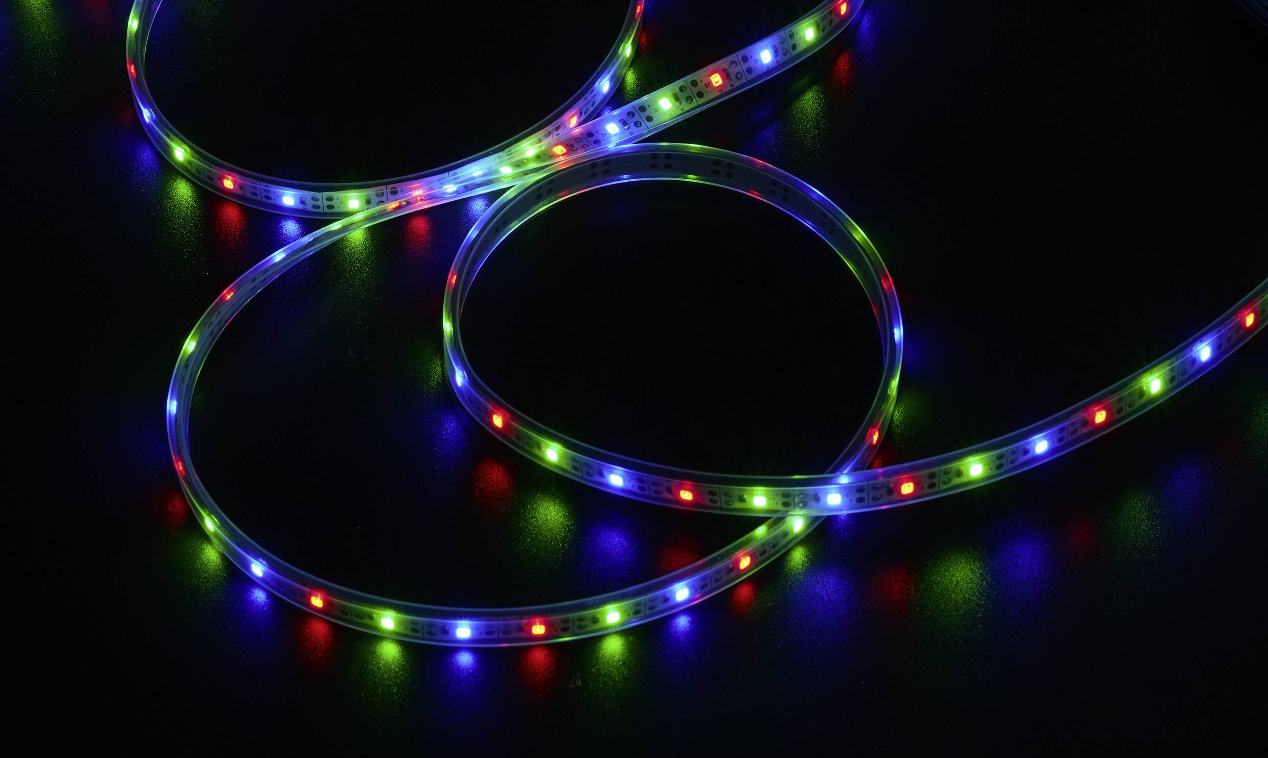 Pasek świateł LED na ciemnym tle, świecący na czerwono, zielono i niebiesko, tworzący pętle i wzory.