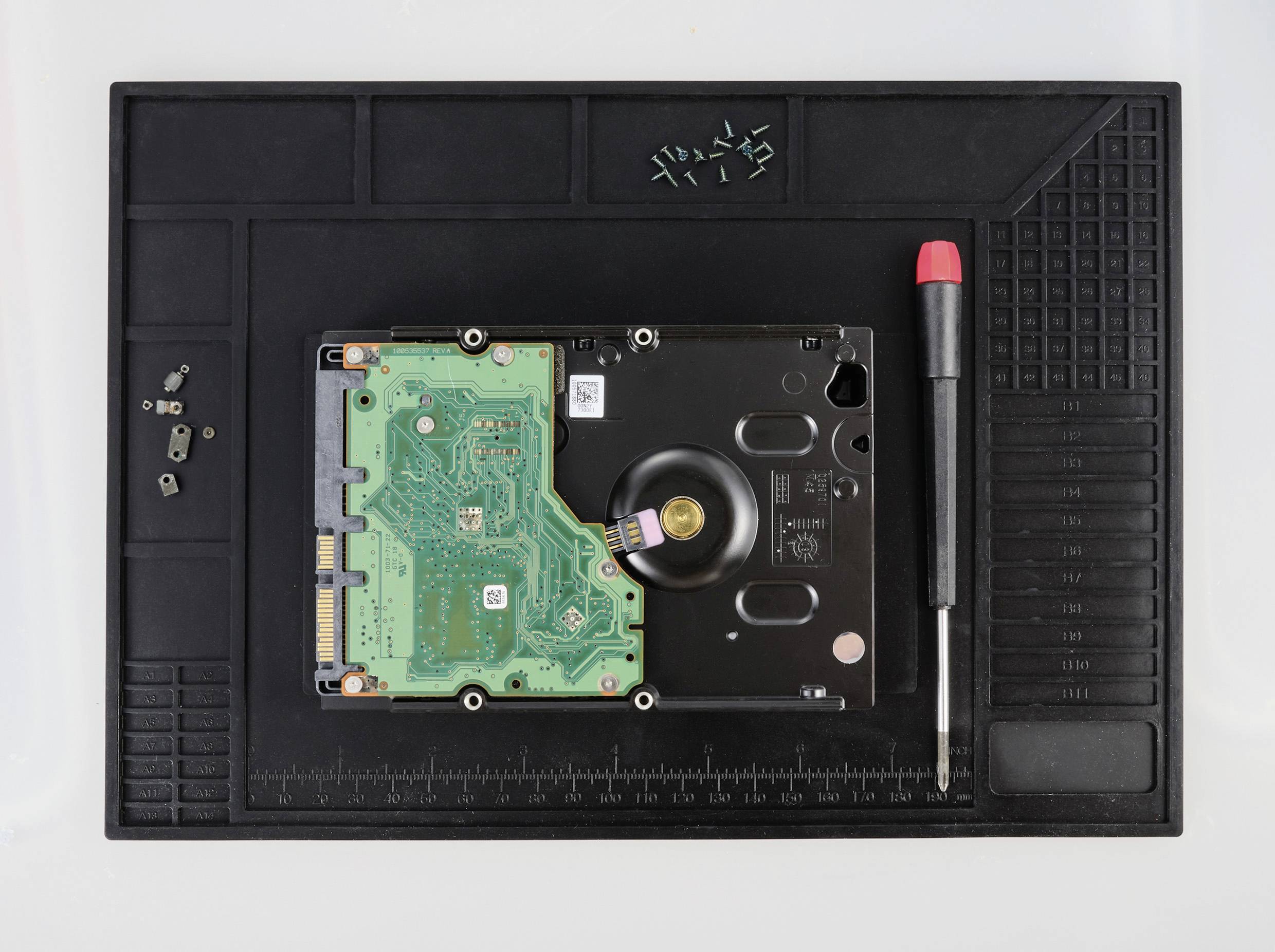 Dysk twardy leży na macie antystatycznej, obok niego śrubokręt i kilka małych śrub.