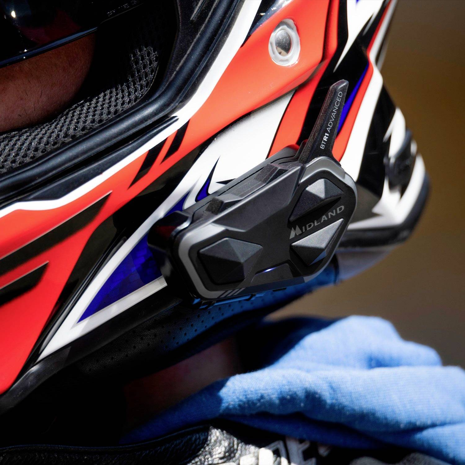 Kask motocyklowy o dynamicznym wzorze w kolorach czarnym, białym i czerwonym. Po boku zamontowane jest urządzenie komunikacyjne.