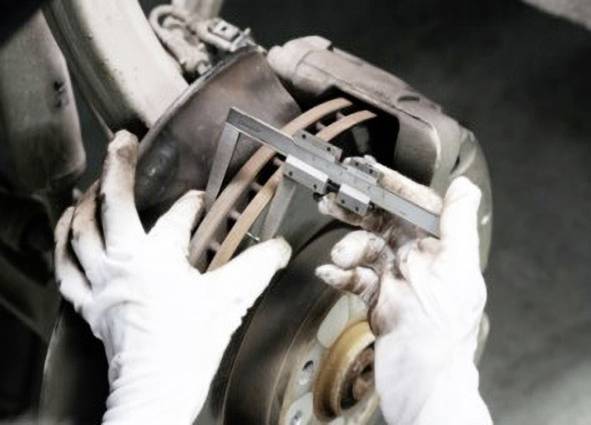 Osoba w białych rękawiczkach mierzy grubość tarczy hamulcowej samochodu suwmiarką.