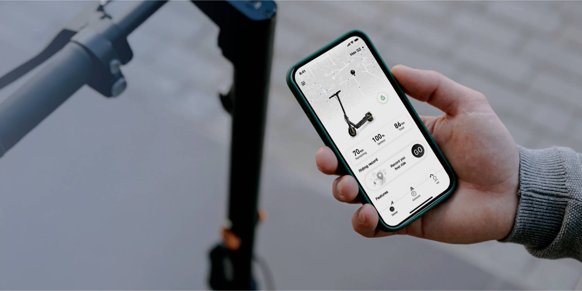 Zbliżenie dłoni trzymającej smartfon z aplikacją hulajnogi elektrycznej. Aplikacja wyświetla mapę, prędkość, przebieg i stan baterii.