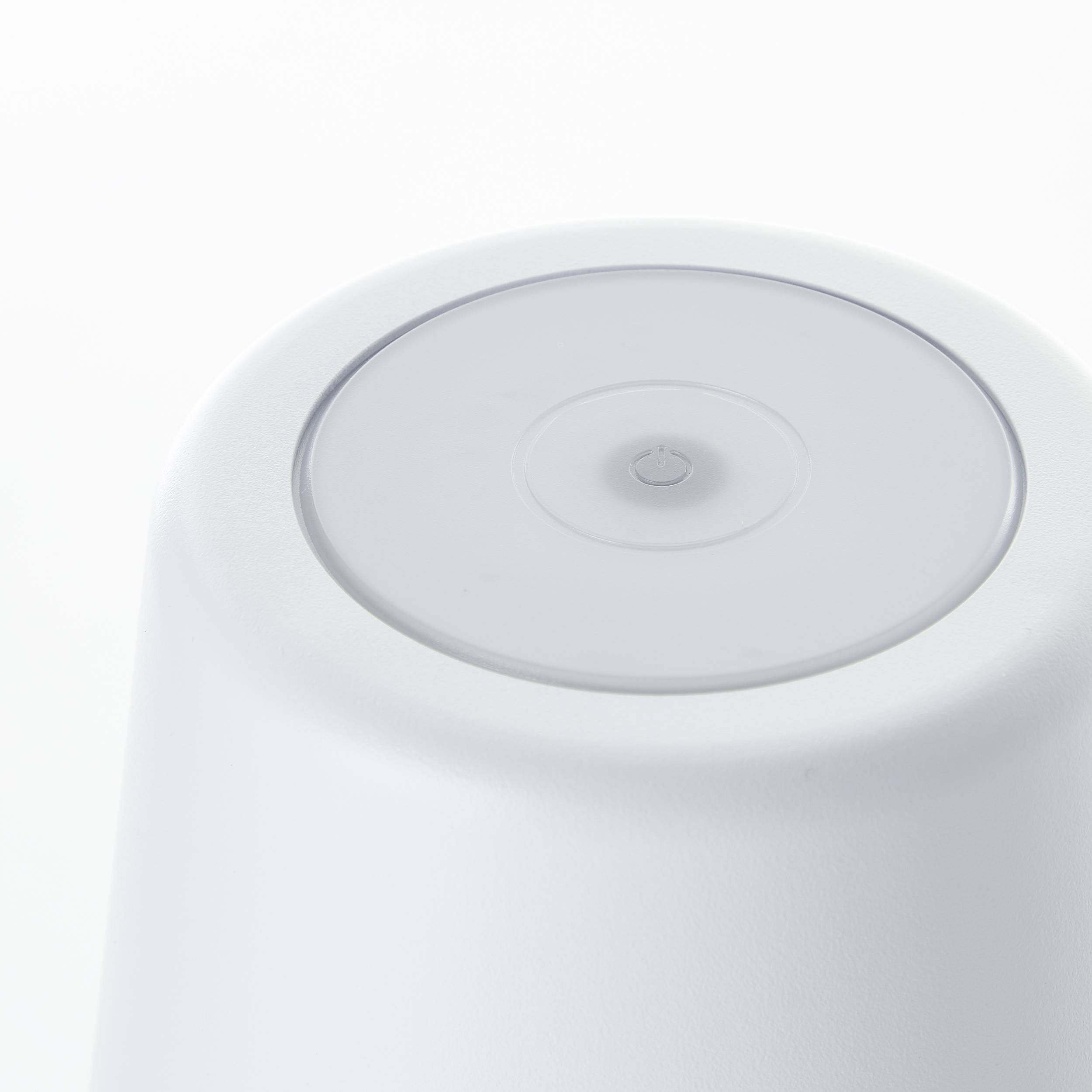 Biały, odwrócony kubek z okrągłą, przezroczystą pokrywką na górze. Kubek posiada gładką powierzchnię.