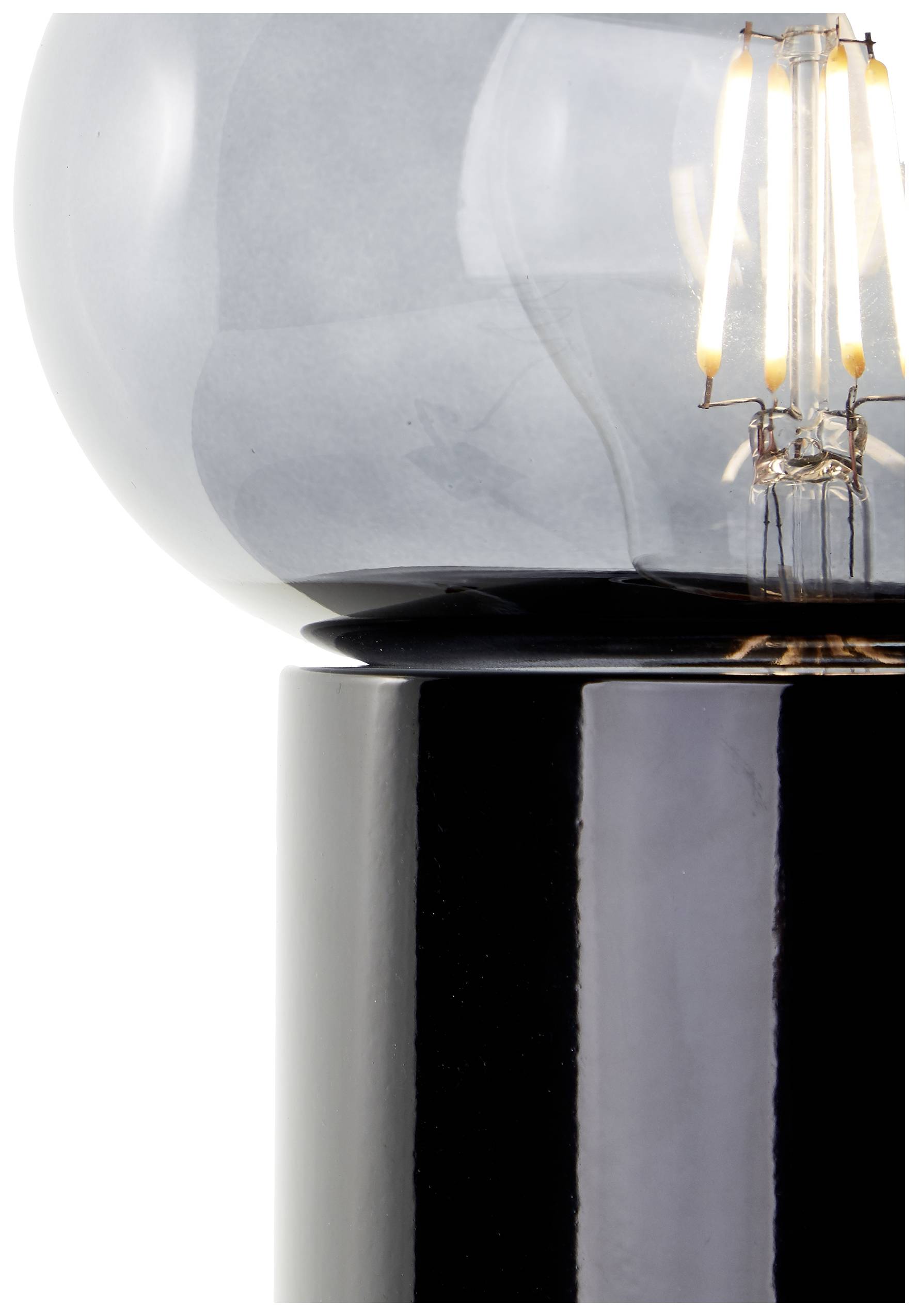 Zbliżenie nowoczesnej lampy stołowej z czarną podstawą i szklaną żarówką, przez którą widoczne są świecące włókna żarowe.