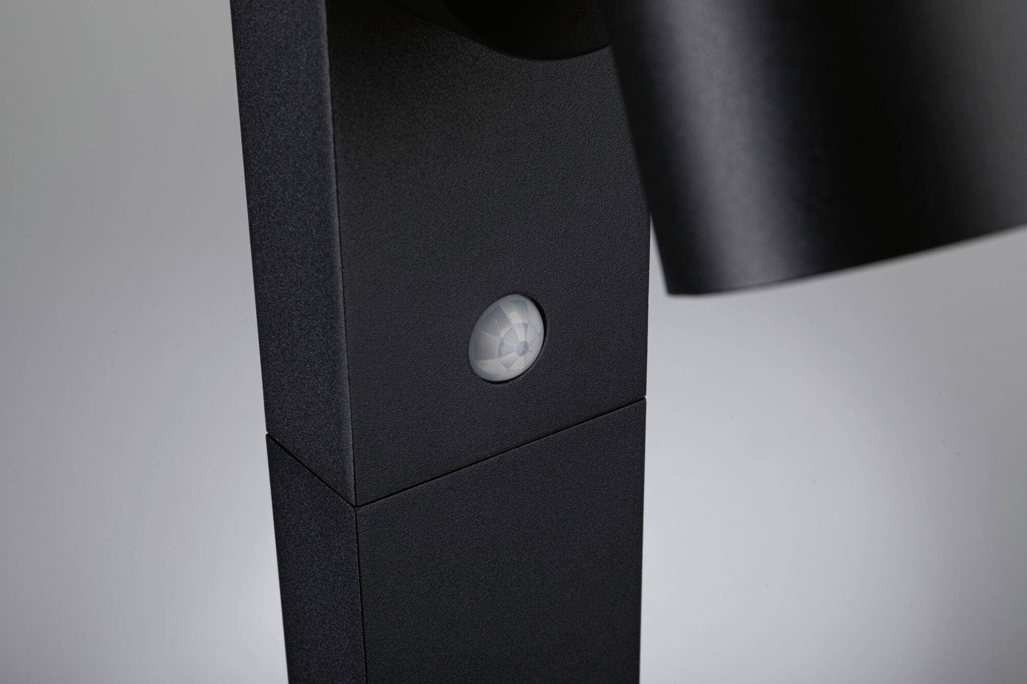 Zbliżenie czujnika ruchu w kolorze czarnym zamontowanego na lampie, wykrywającego ruch w pomieszczeniu.