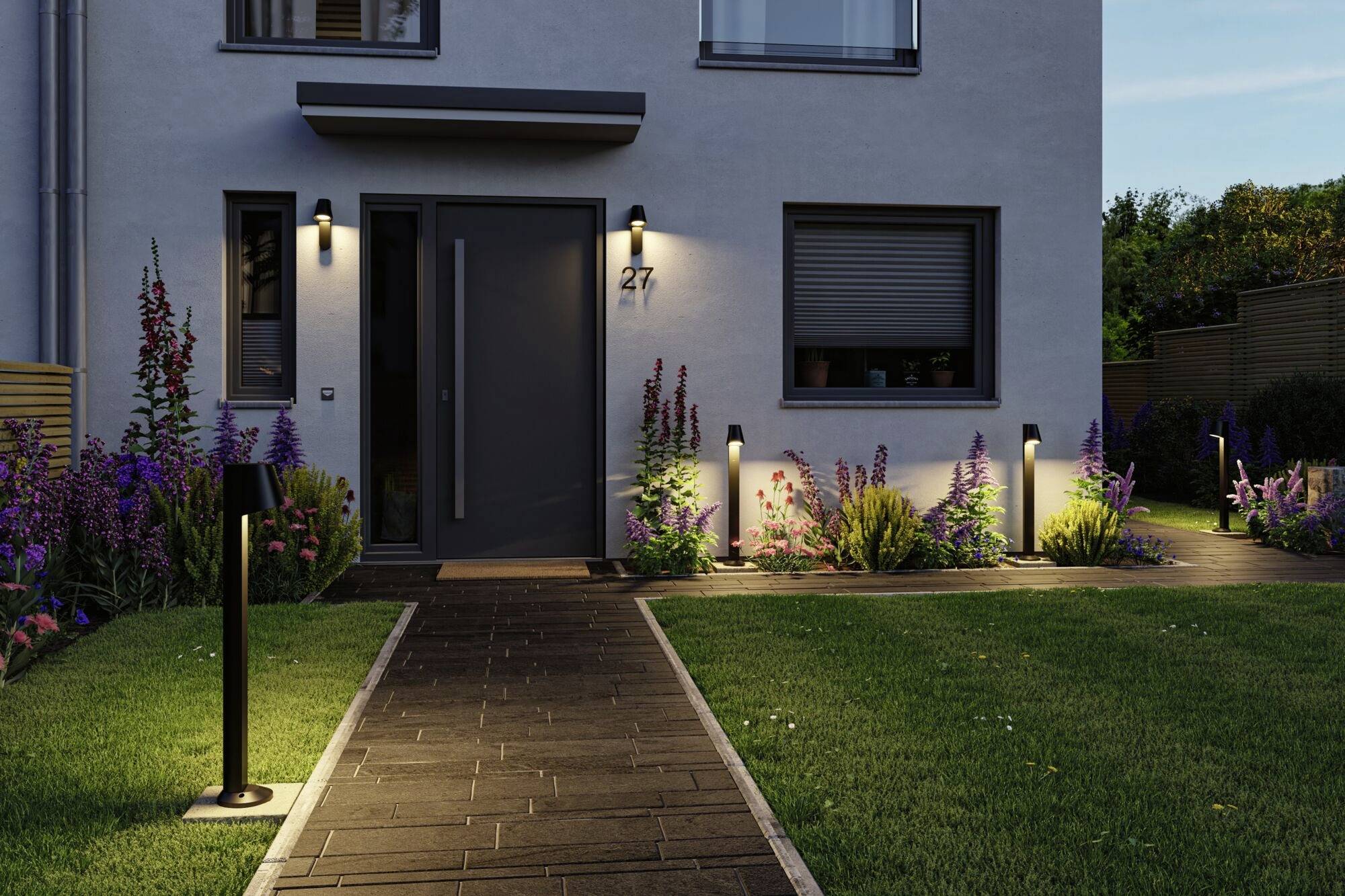 Nowoczesny dom z podświetlonym wejściem; ścieżka z latarniami, otoczona rabatkami kwiatowymi.