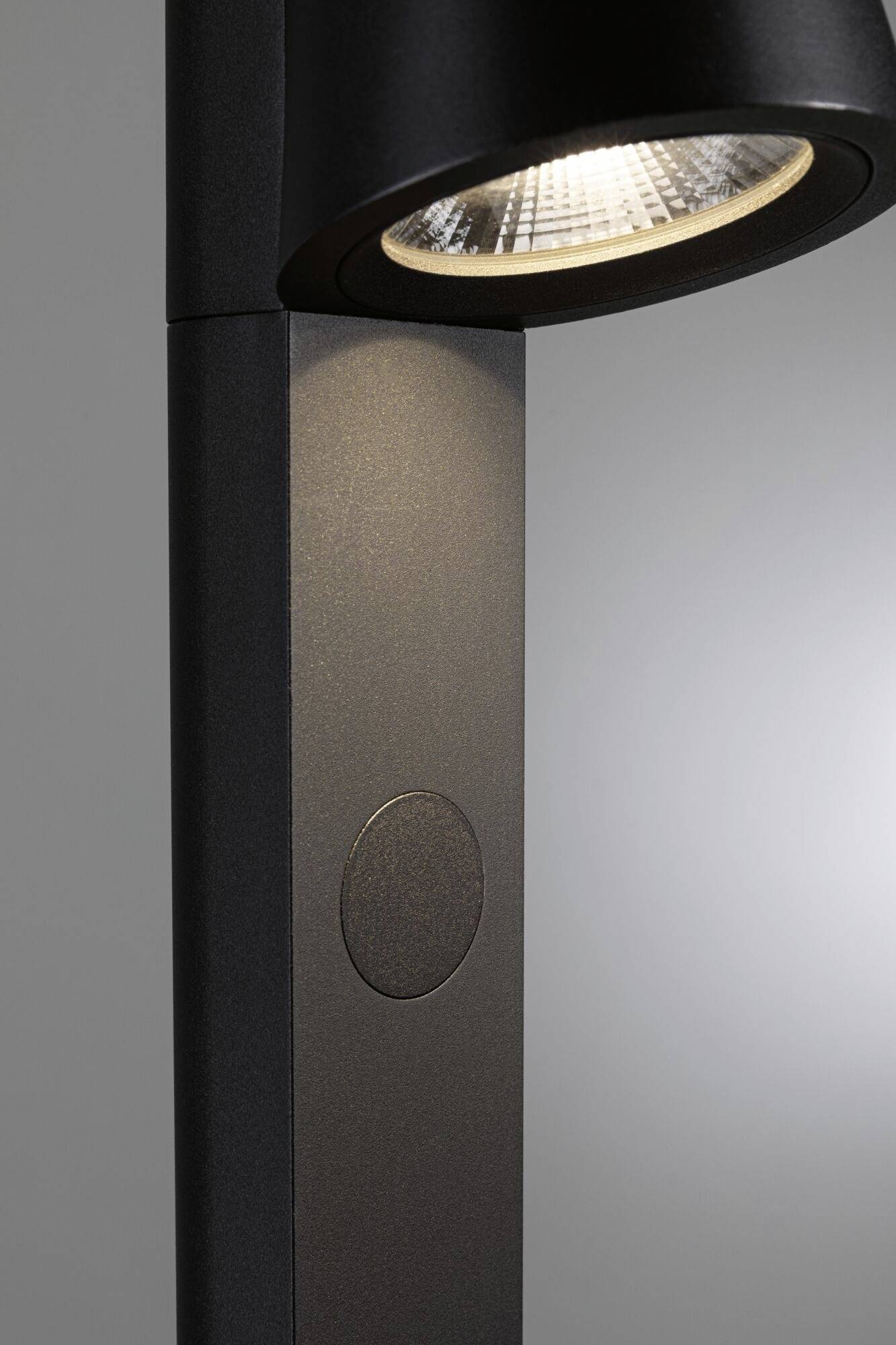 Nowoczesna, czarna lampa stojąca o prostym designie, rzucająca światło na ścianę, podkreśla elegancki, minimalistyczny wygląd.