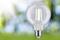 Żarówka symbolizująca energię i innowację na rozmytym tle w odcieniach zieleni i błękitu, z promieniami słonecznymi.