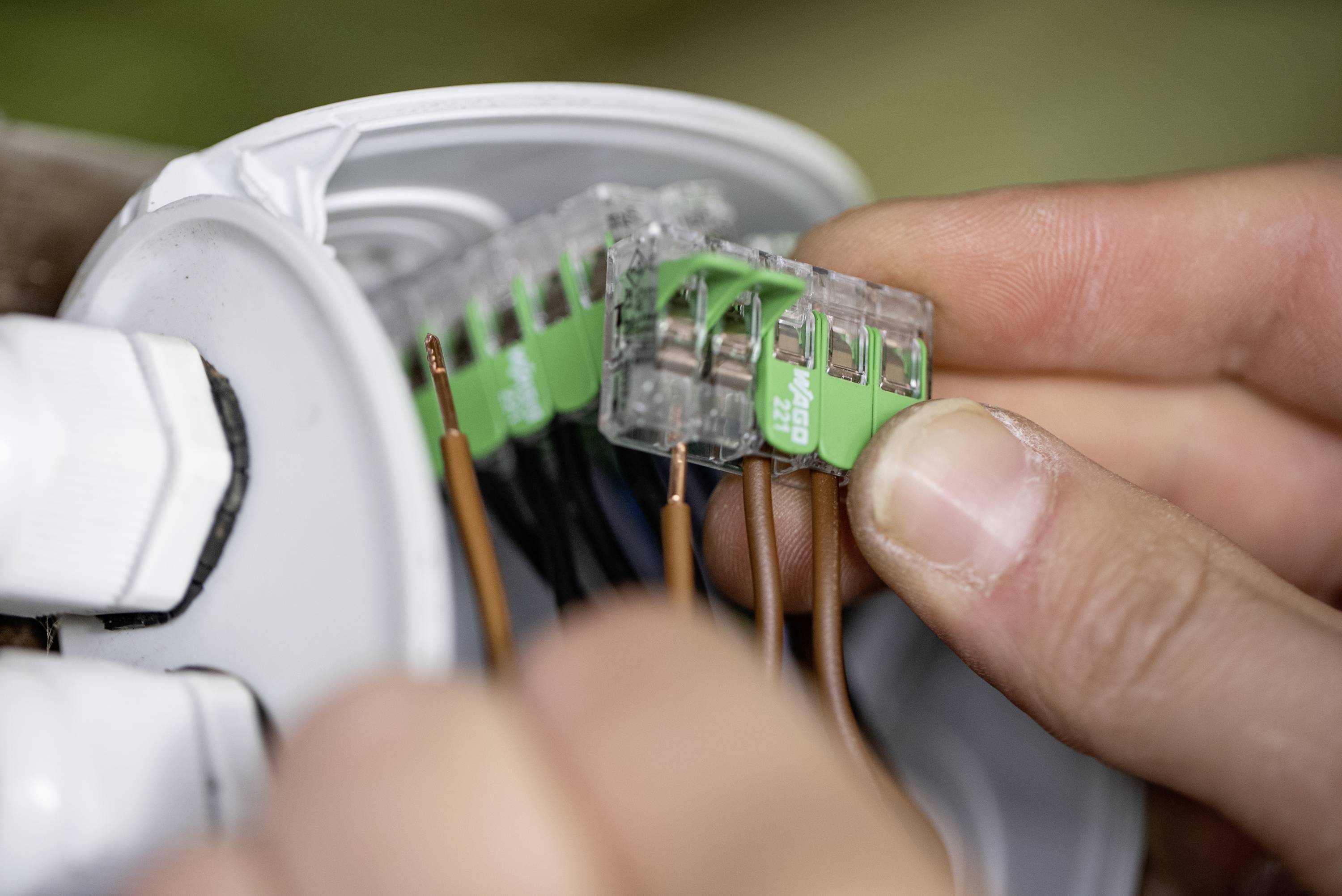 Zbliżenie na dwie ręce wprowadzające przewody do puszki elektrycznej, ilustrujące proces podłączania.