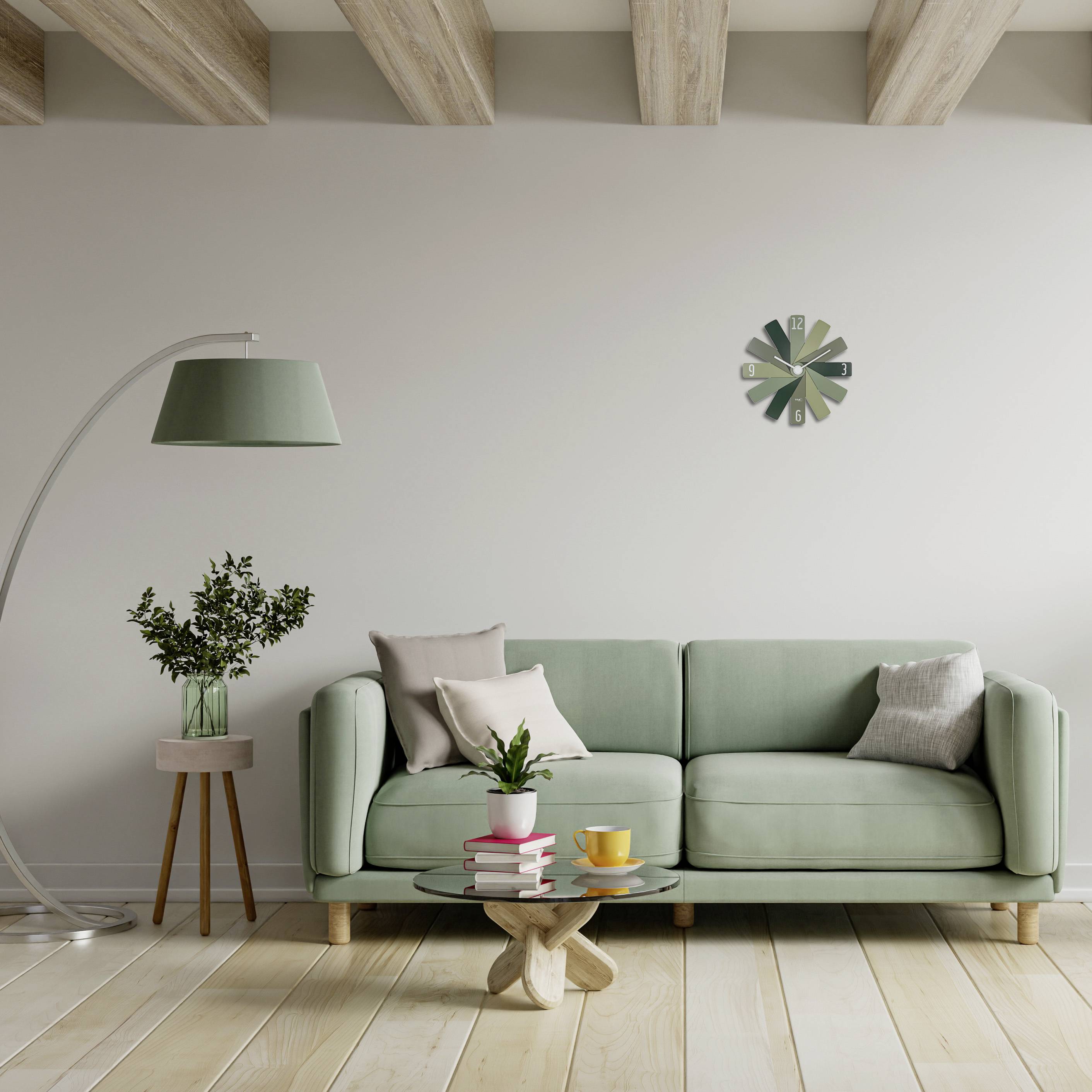 Salon z zieloną sofą, okrągłym drewnianym stolikiem z filiżankami, lampą stojącą, rośliną i zegarem ściennym.