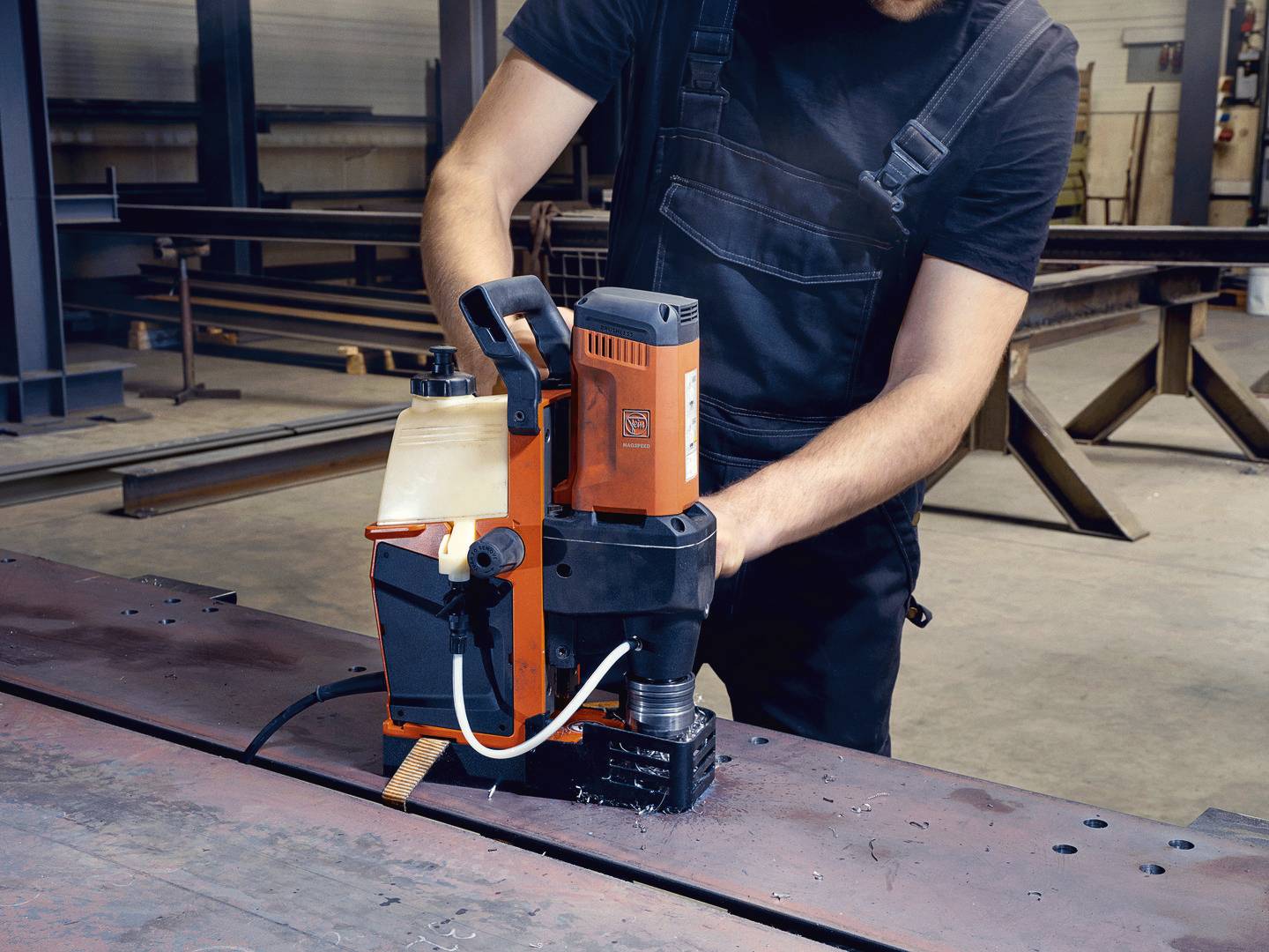 Robotnik obsługuje wiertarkę magnetyczną na metalowym stole w środowisku warsztatu.