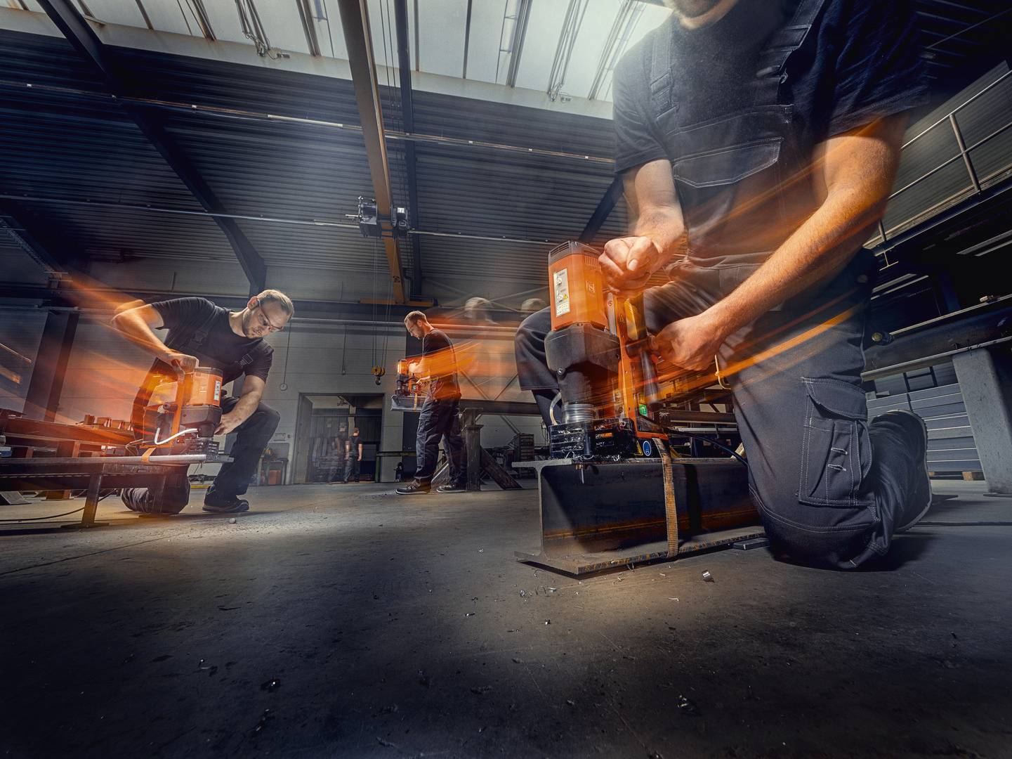 Robotnicy w hali fabrycznej obsługują maszyny do obróbki metalu. Scena ukazuje dynamikę pracy i zastosowanie zaawansowanych technologii.