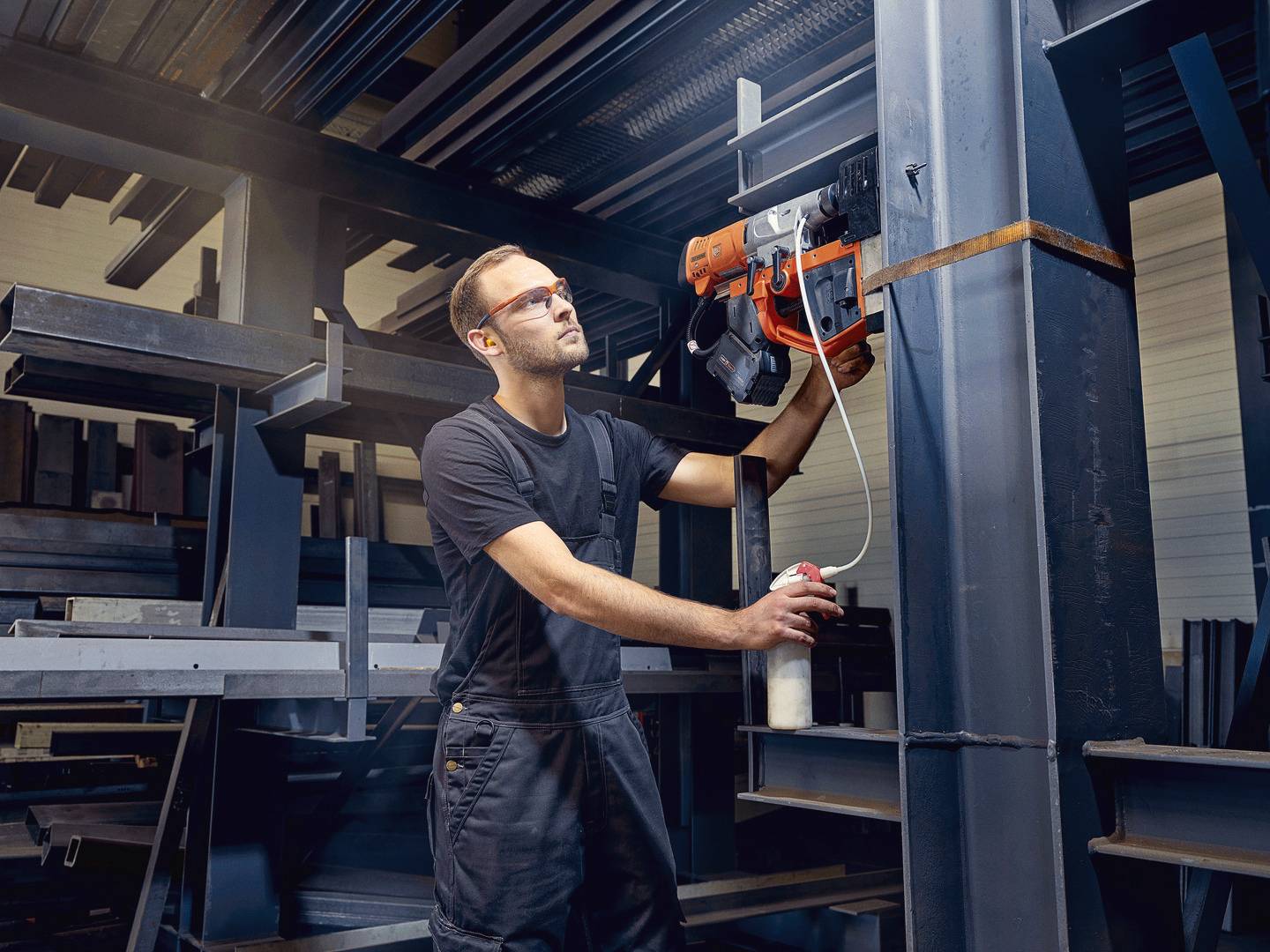Mężczyzna w ubraniu roboczym sprawdza maszynę w środowisku fabrycznym, trzymając w ręku spray wspomagający konserwację.