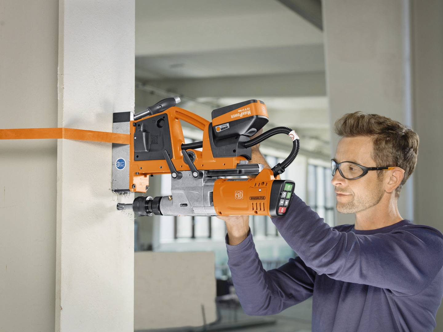 Mężczyzna używa elektronarzędzia, aby wywiercić otwór w ścianie. Ma na sobie okulary ochronne i wygląda na skupionego.