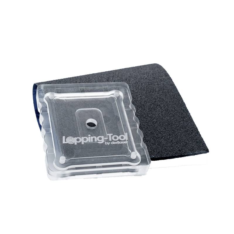 Kwadratowe narzędzie do szlifowania z przezroczystą obudową leży na czarnej podkładce szlifierskiej. Tekst na narzędziu: 'Narzędzie do docierania'.