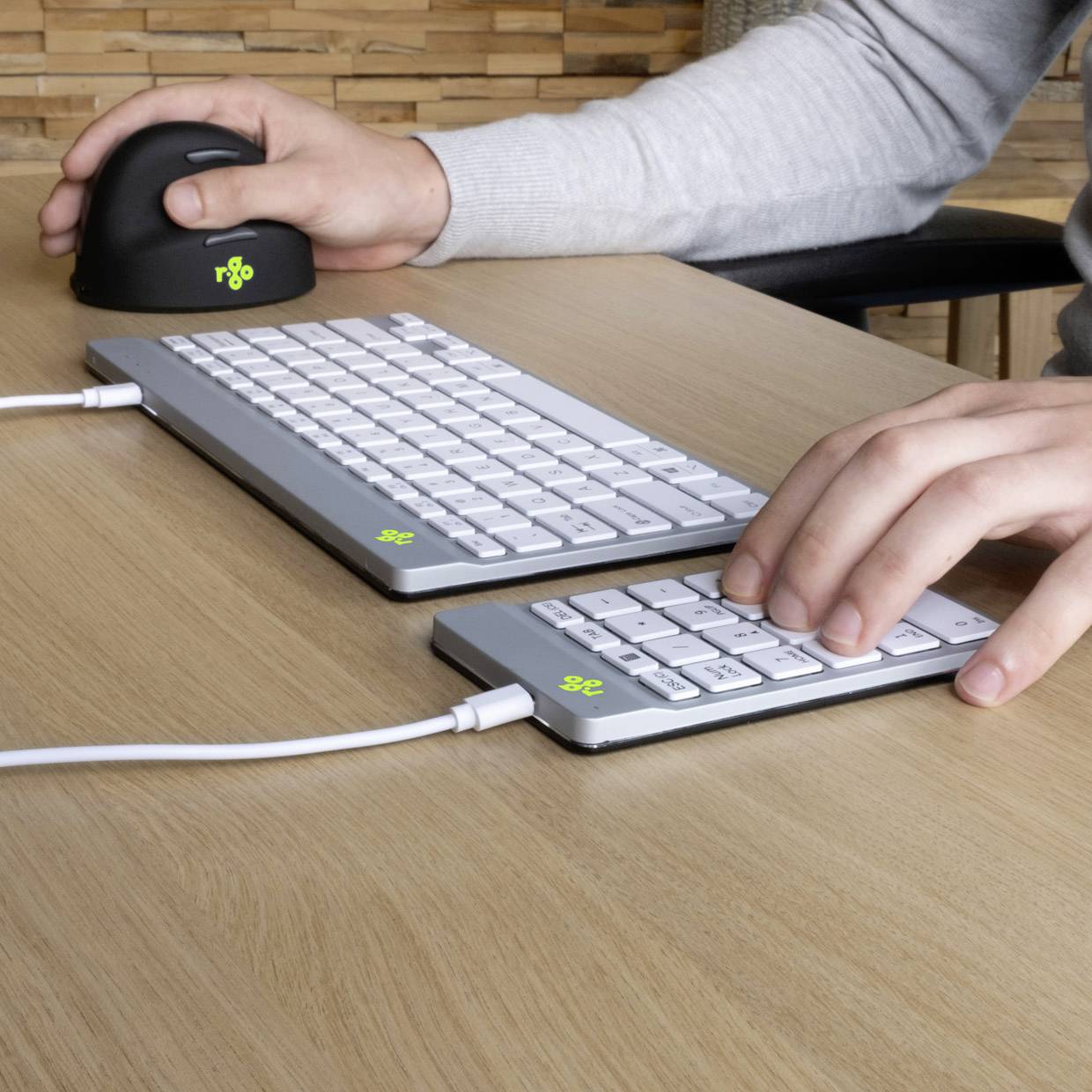 Osoba pisze na kompaktowej klawiaturze i przesuwa ergonomiczną mysz po drewnianym stole.