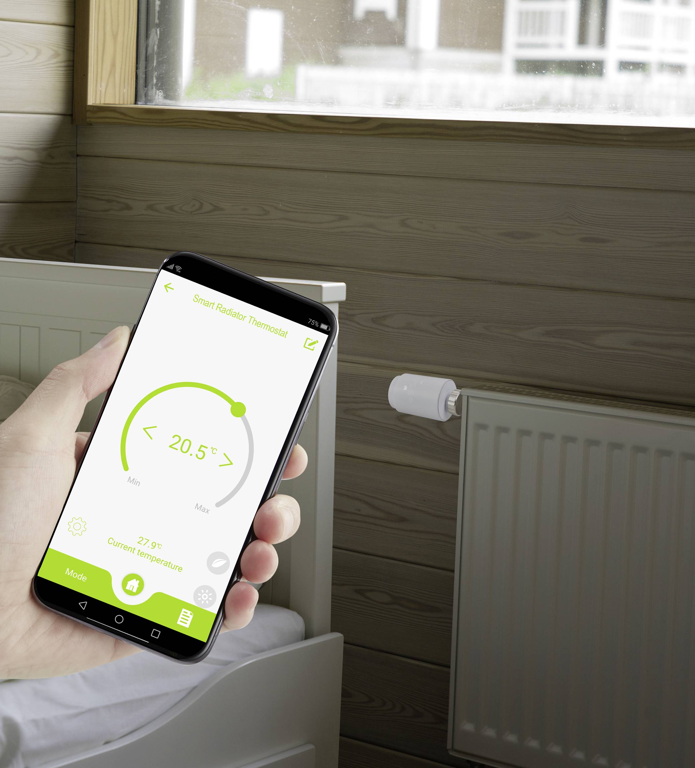 Jedna ręka trzyma smartfon wyświetlający aplikację sterowania inteligentnym termostatem. Na ekranie widać '20,5°C'. W tle znajduje się łóżko i grzejnik.