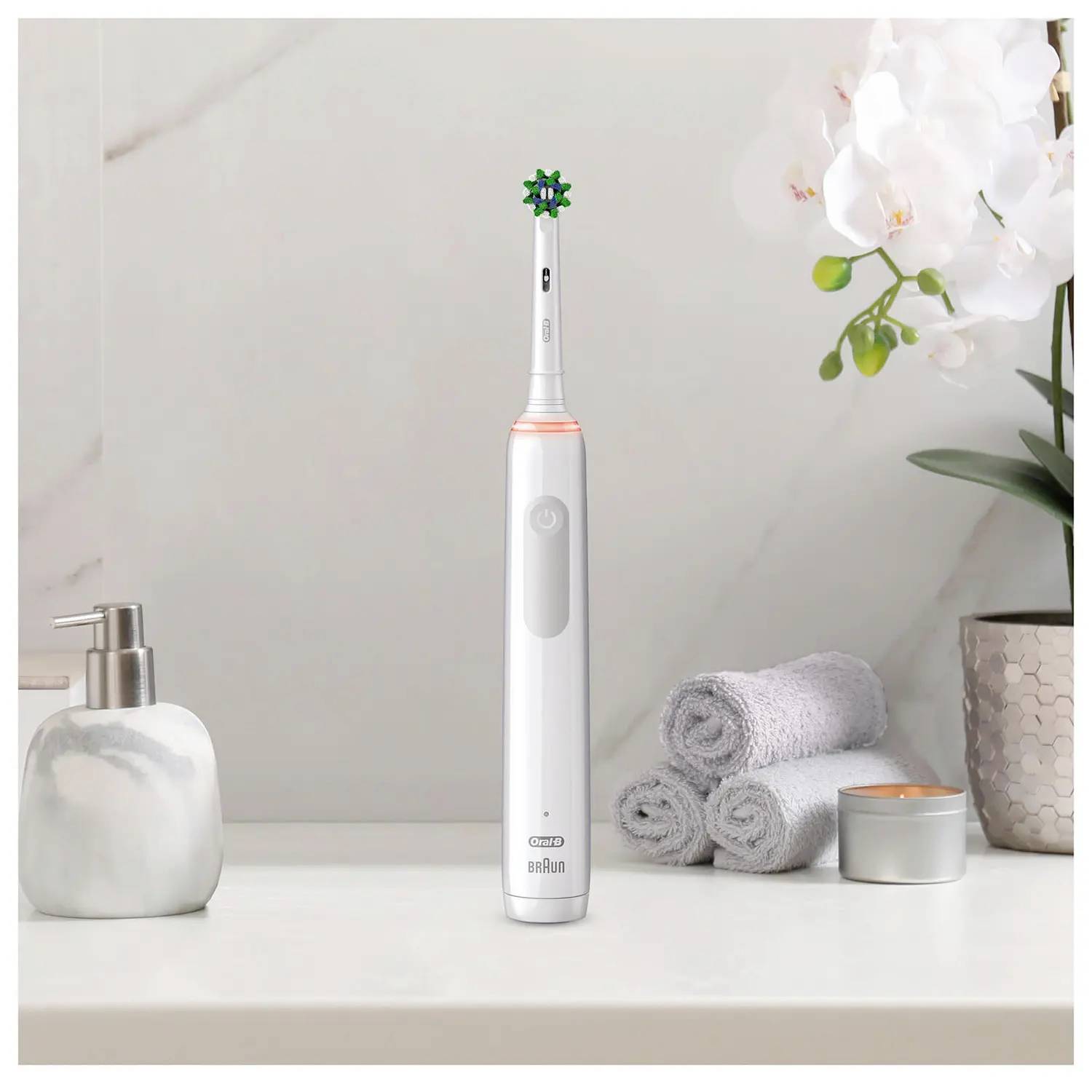 Elektryczna szczoteczka do zębów na półce łazienkowej obok dozownika mydła, złożonych ręczników i orchidei.